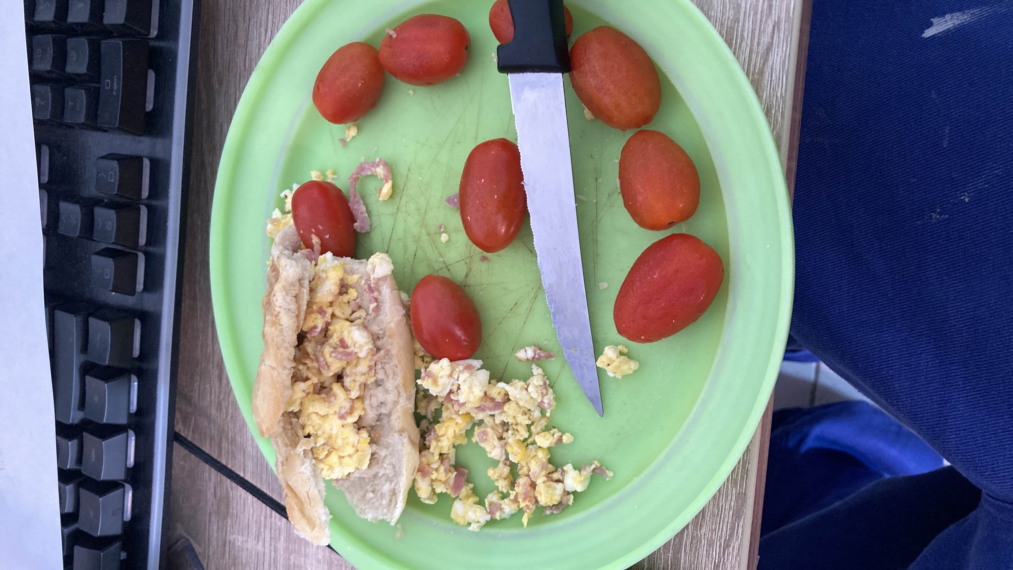 A plate containing a bread roll filled with scrambled eggs and ham, accompanied by cherry tomatoes.