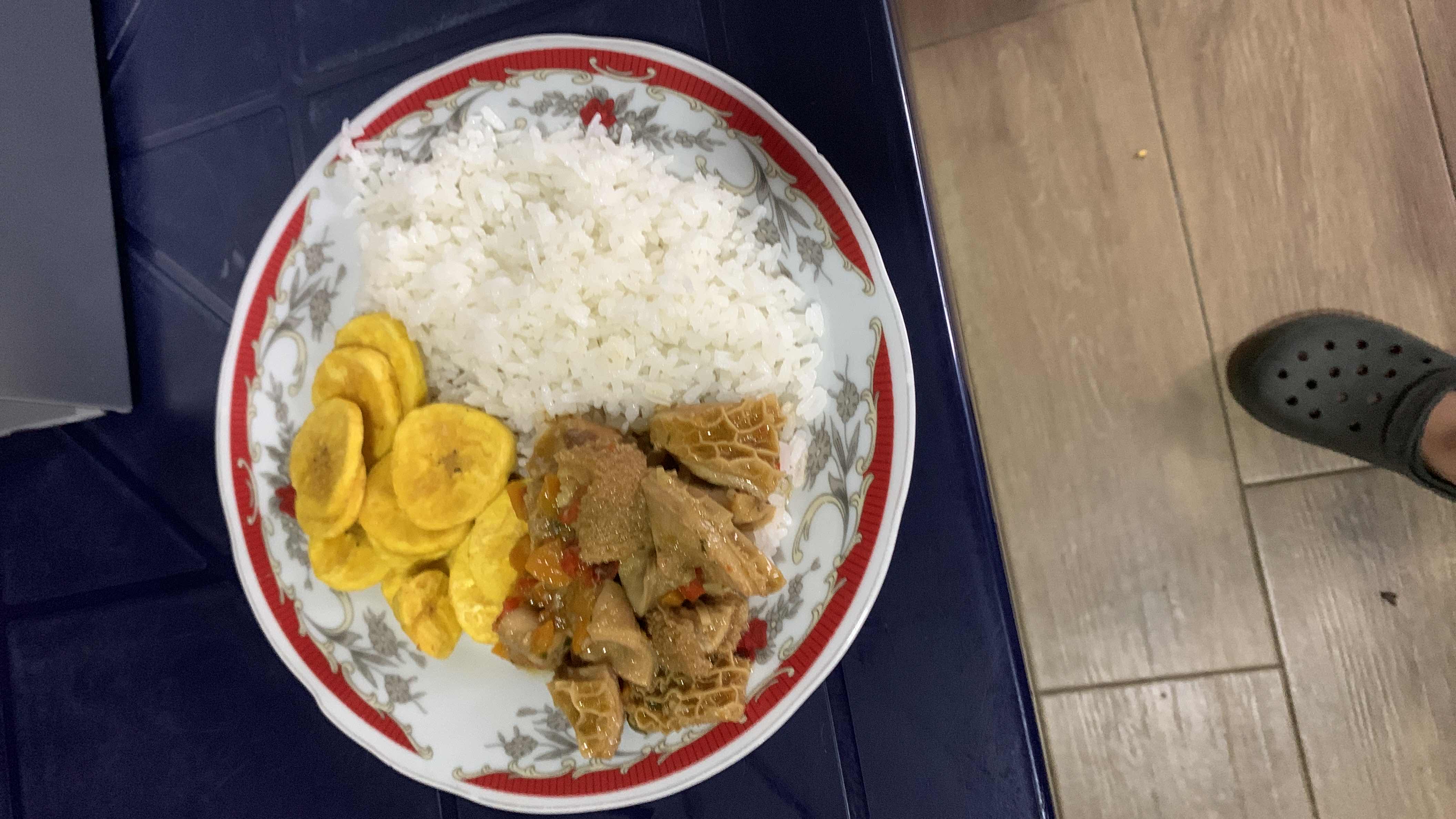 A plate containing white rice, fried plantains, and stewed tripe, offering a balanced mix of carbohydrates, protein, and fats.
