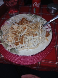 A plate of spaghetti with meat sauce and parmesan cheese, served with a drink.