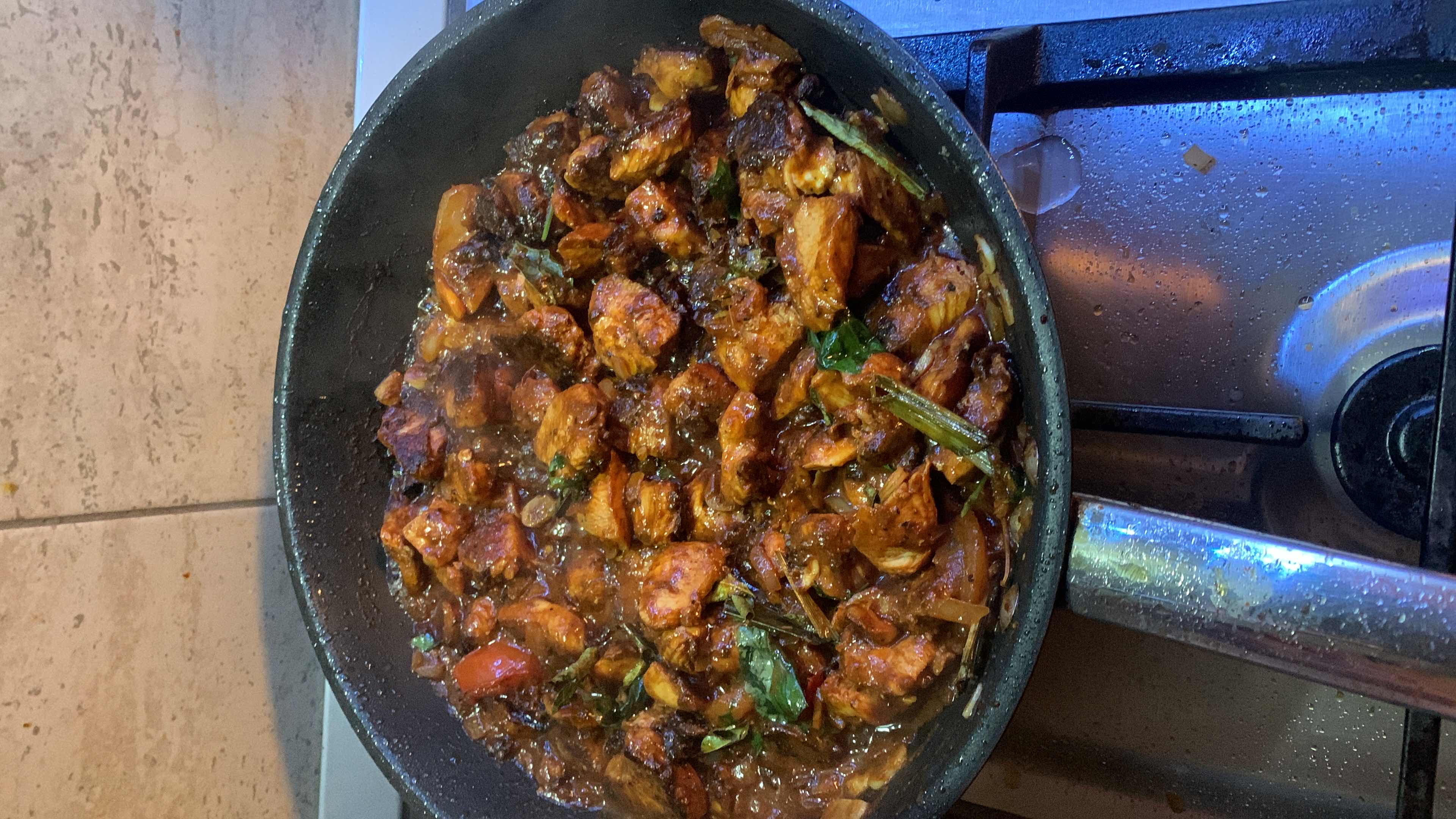 A spicy chicken stir-fry dish cooked with onions, tomatoes, and aromatic spices, providing a balanced mix of protein, carbs, and fats.
