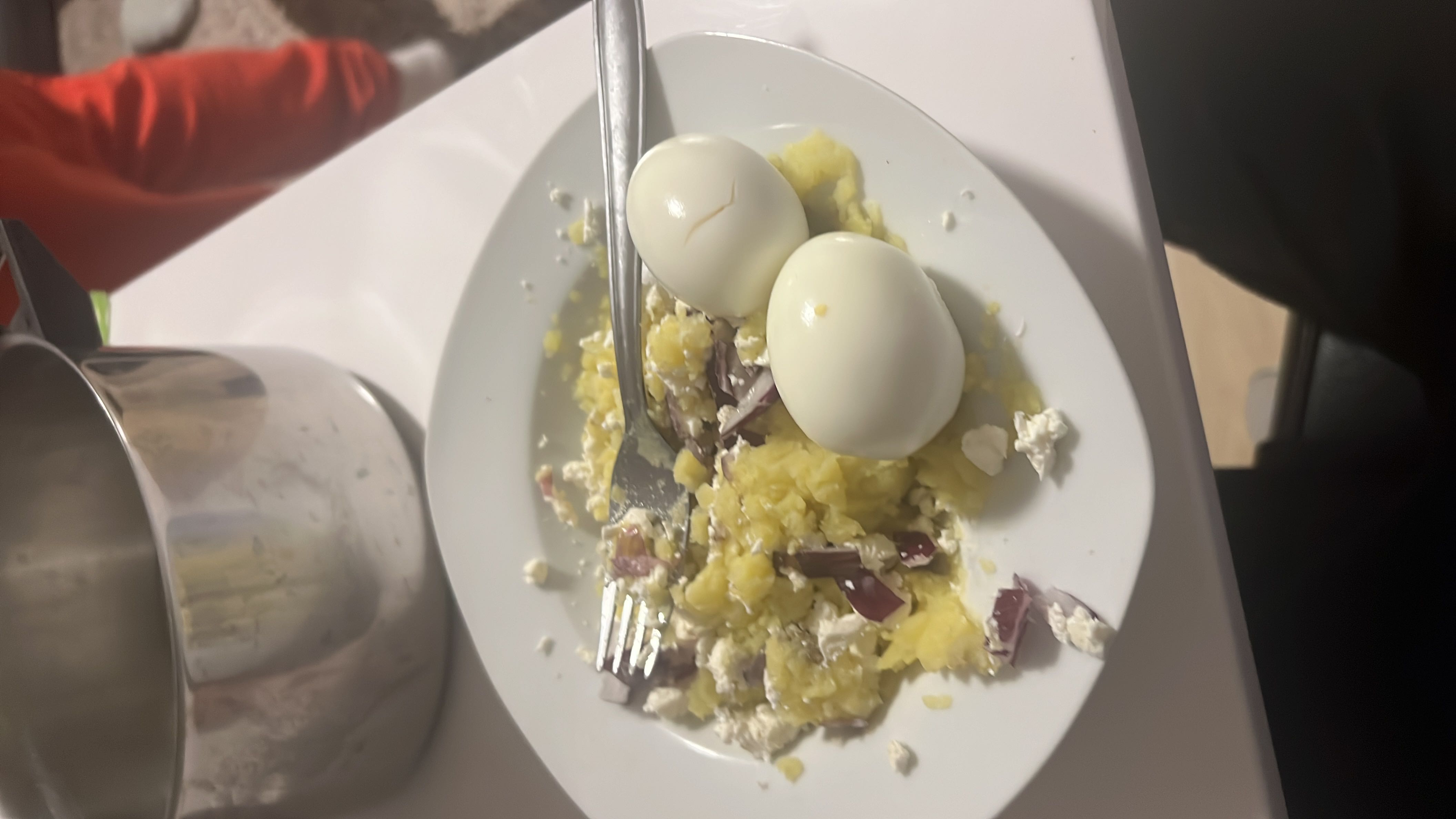 A plate containing two boiled eggs, mashed potatoes, red onion, and crumbled feta cheese, providing a balanced mix of protein, carbs, and fats.