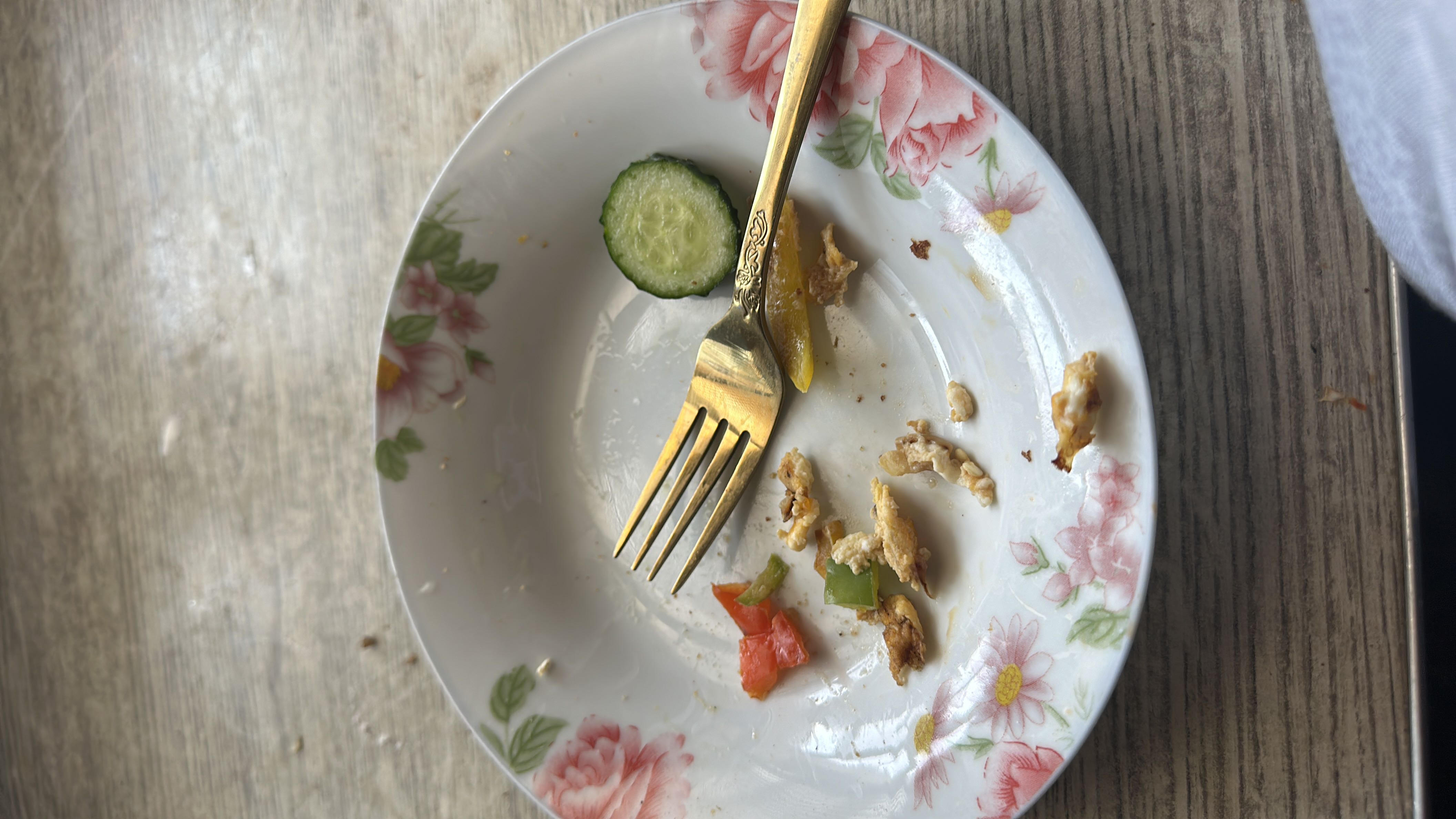 The plate contains remnants of a light meal, including a cucumber slice, tomato, green pepper, and scrambled egg bits, with an estimated total of 50 calories.