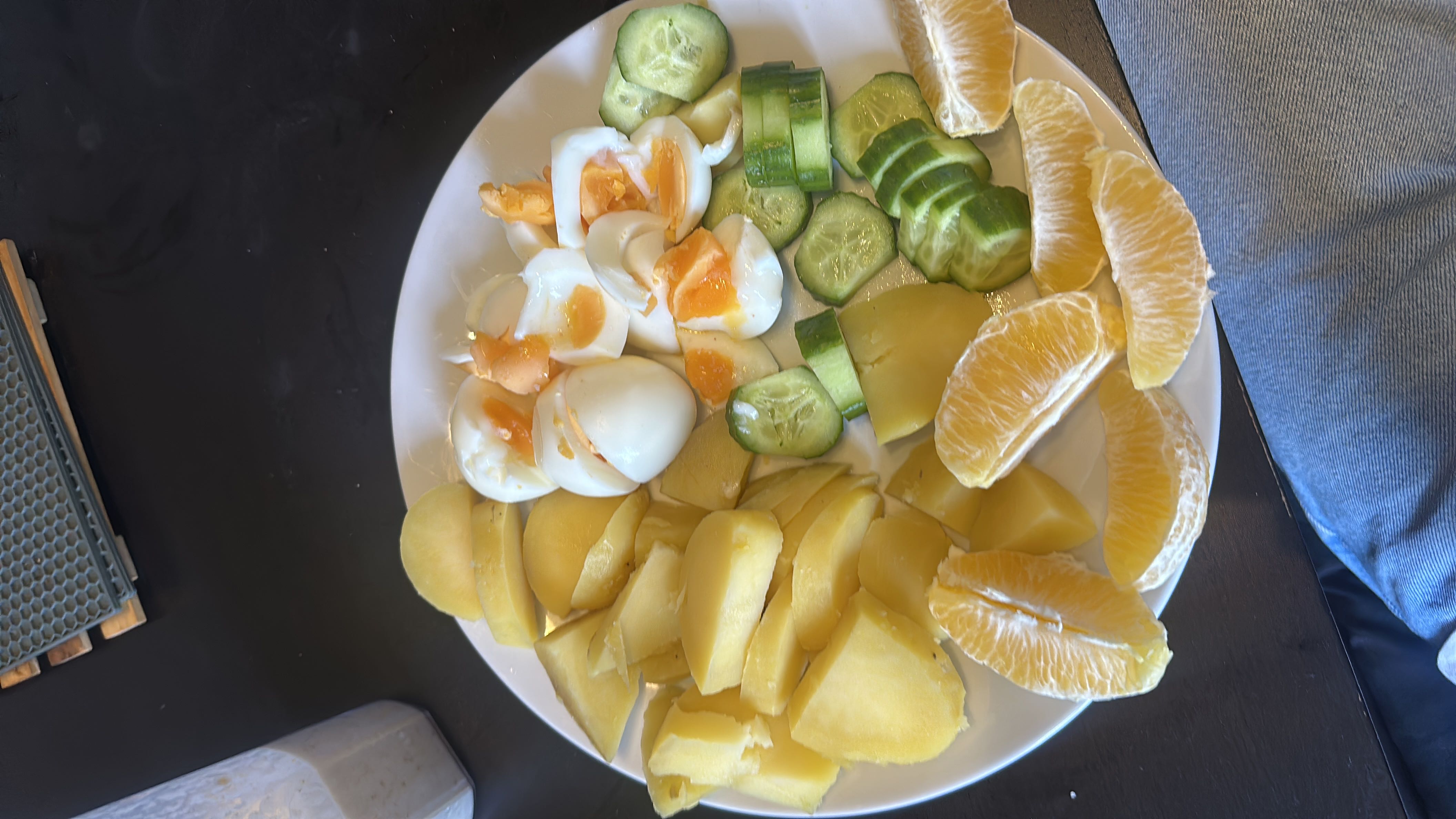 A balanced meal consisting of boiled eggs, potatoes, cucumber slices, and orange slices, providing a mix of protein, carbohydrates, and vitamins.