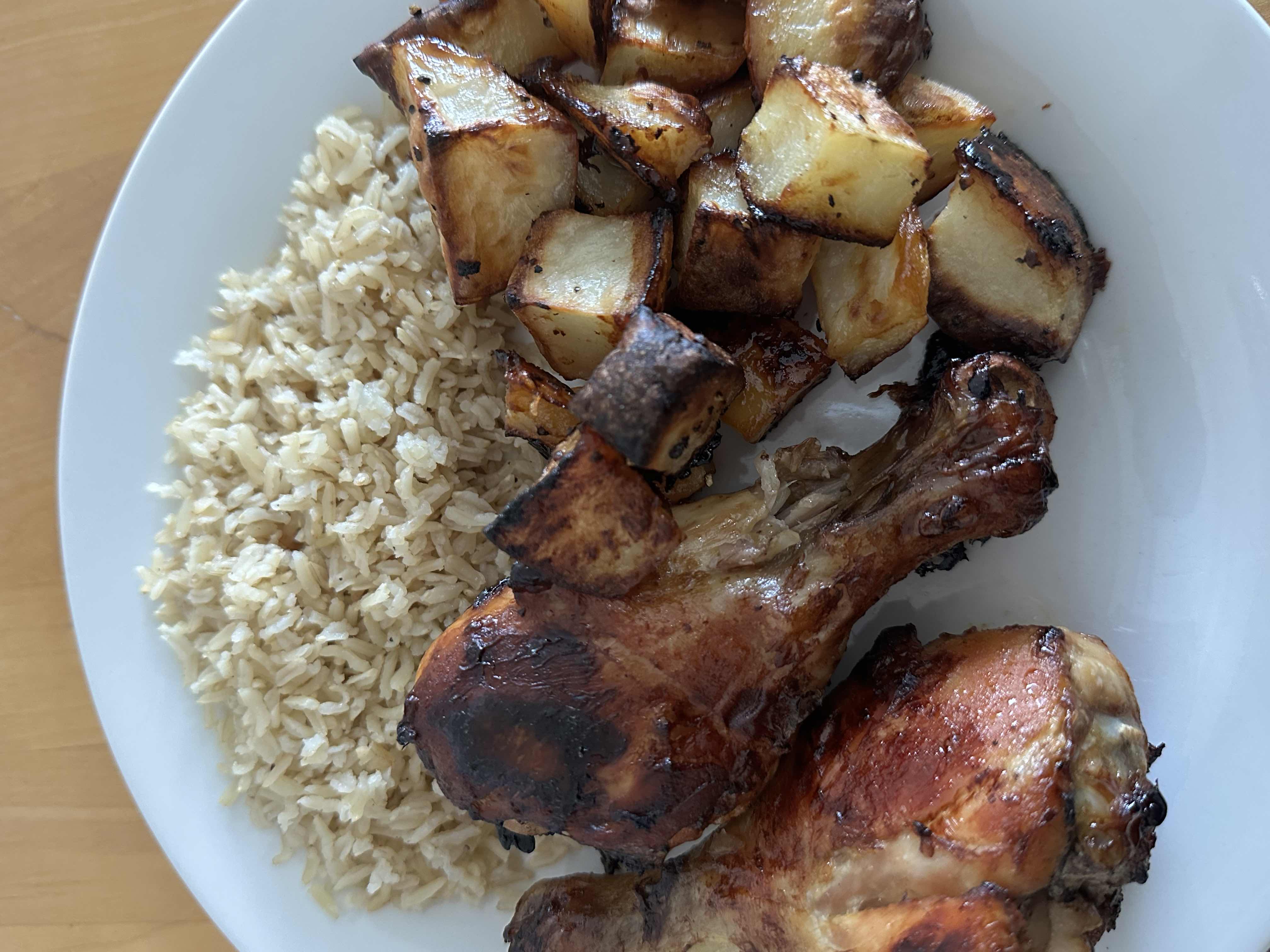 A balanced meal consisting of roasted chicken drumsticks, brown rice, and roasted potatoes.