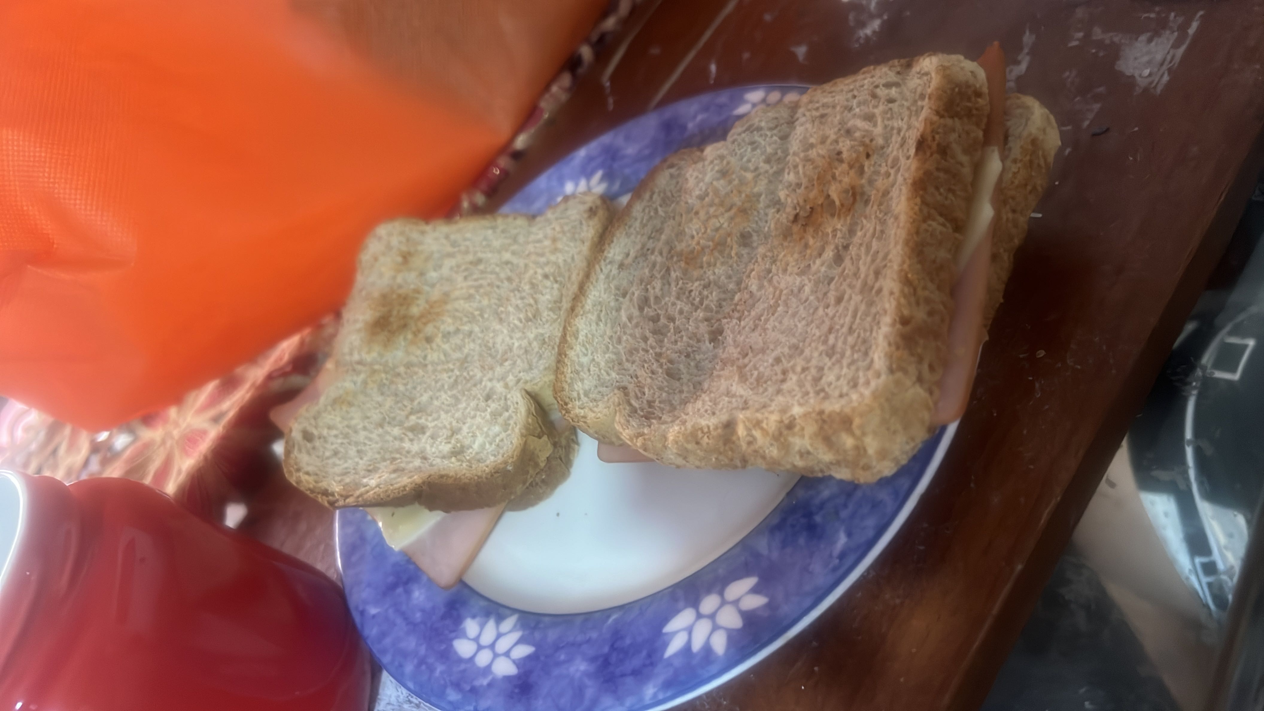 A sandwich made with whole wheat bread, ham, and cheese, served on a plate.