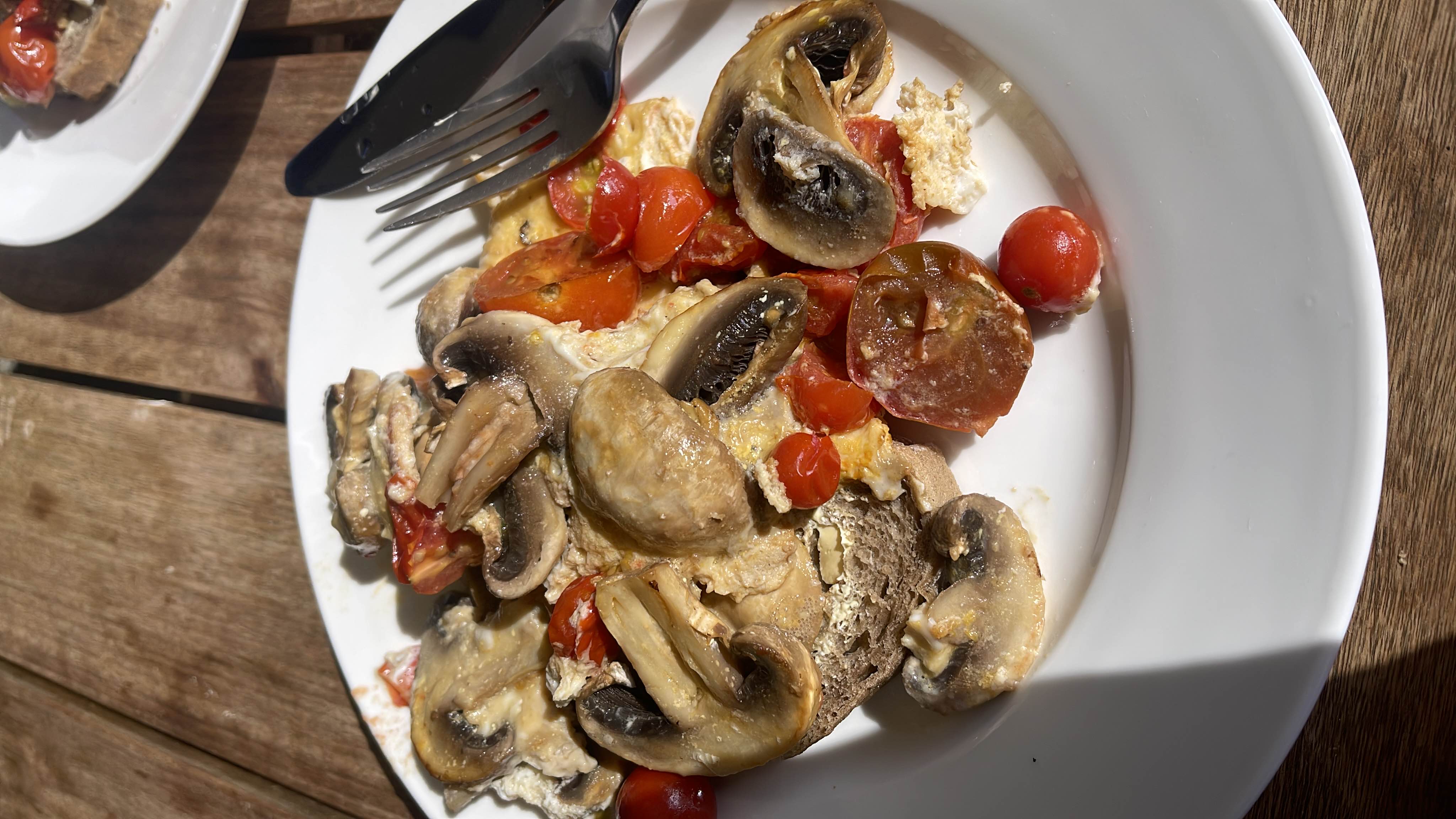 A healthy dish consisting of sautéed mushrooms, cherry tomatoes, eggs, and bread, providing a balanced mix of protein, carbs, and fats.