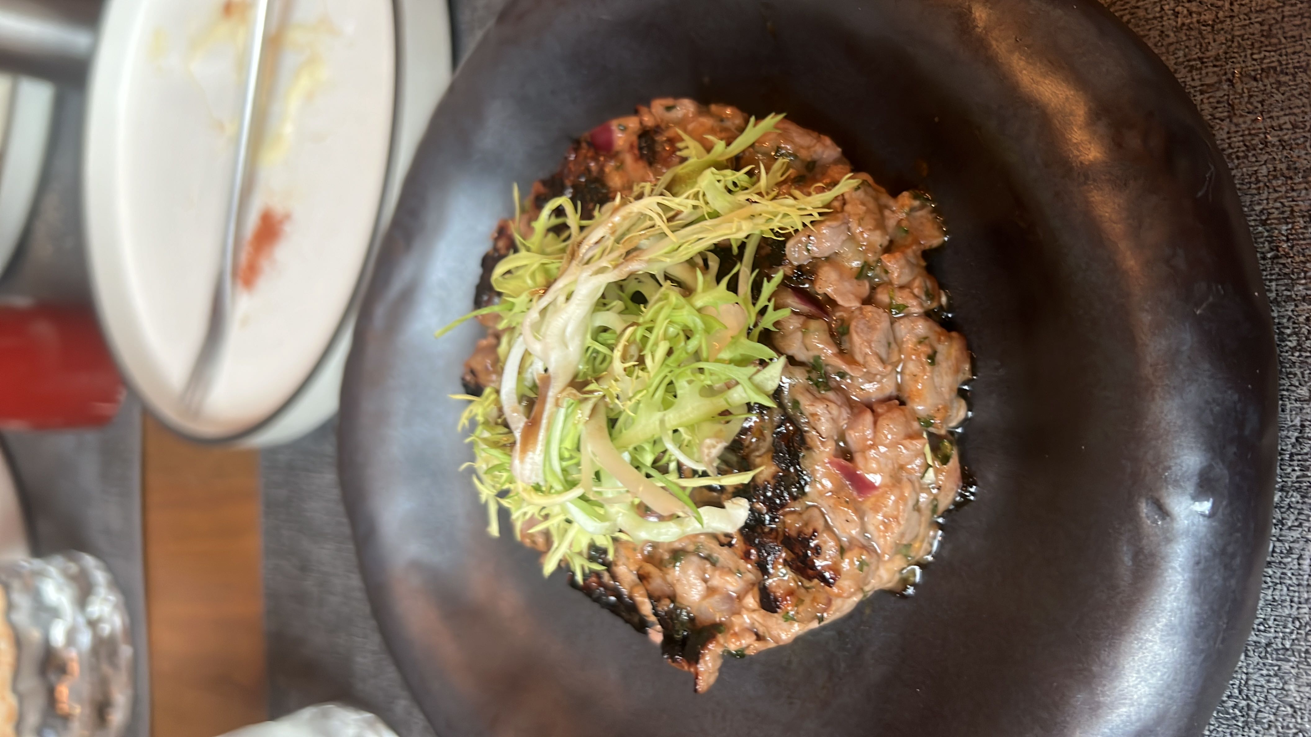 A dish of beef tartare topped with frisée lettuce and herbs, offering a high-protein, moderate-fat meal with minimal carbohydrates.