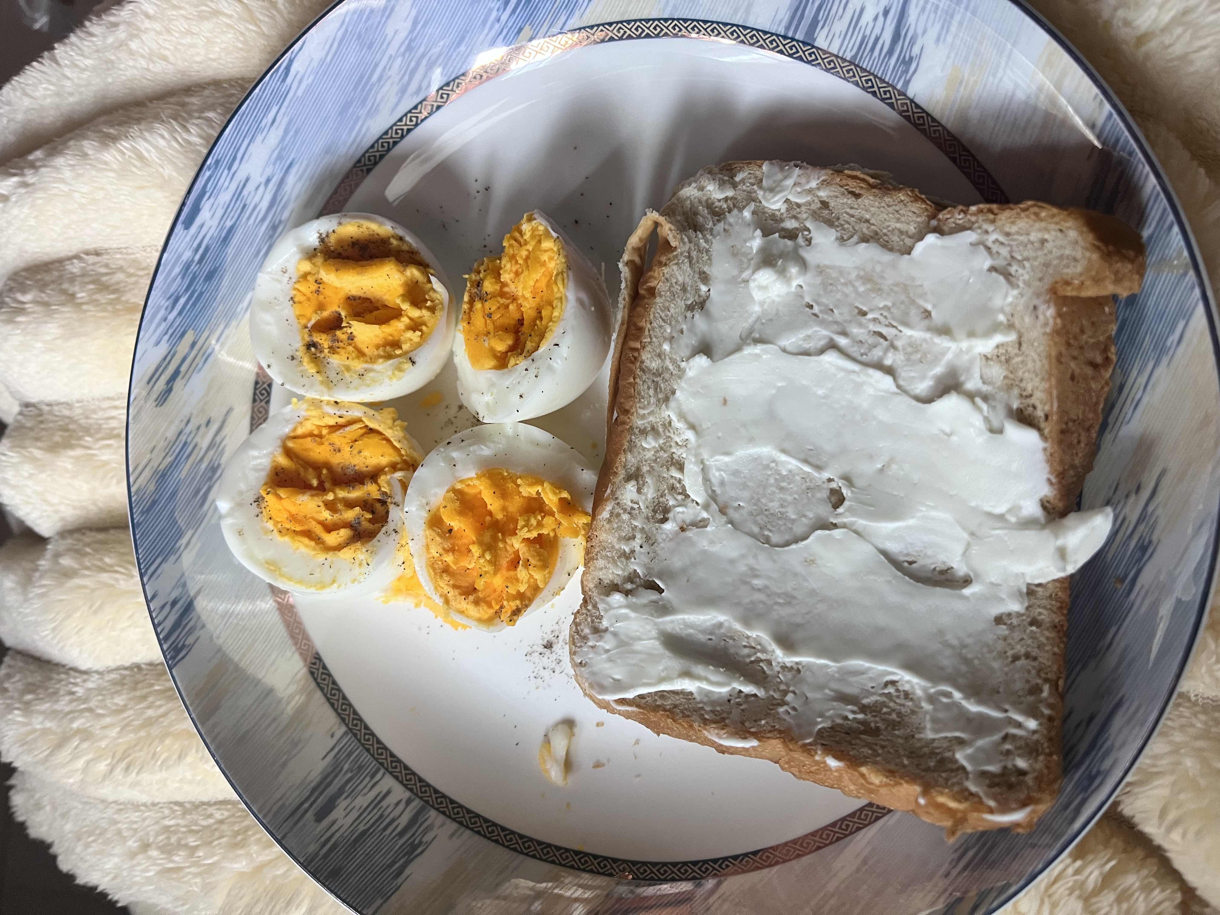 A plate containing boiled eggs and a slice of bread with cream spread, providing a balanced mix of protein, carbs, and fats.