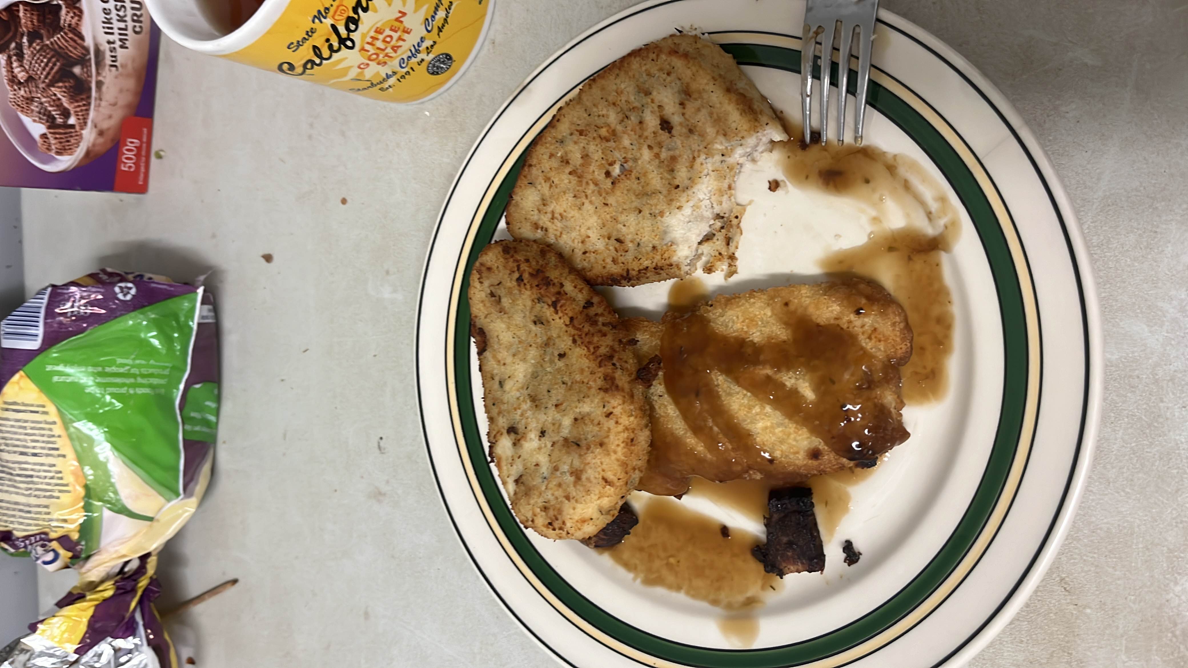 A plate containing breaded chicken cutlets with gravy, accompanied by a small burnt bread piece.