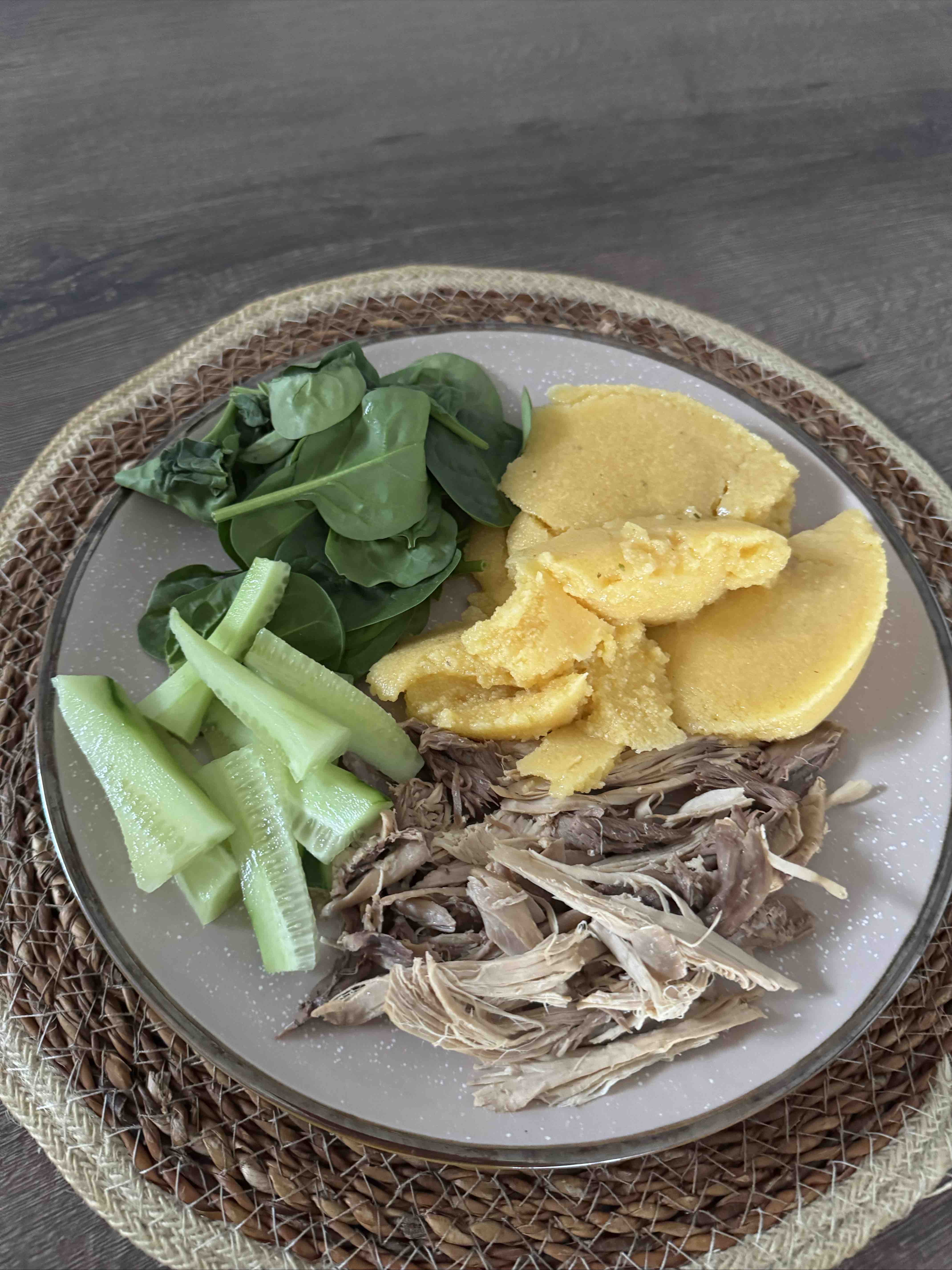 A balanced meal consisting of spinach, cucumber, polenta, and shredded chicken, providing a mix of protein, carbs, and fats.