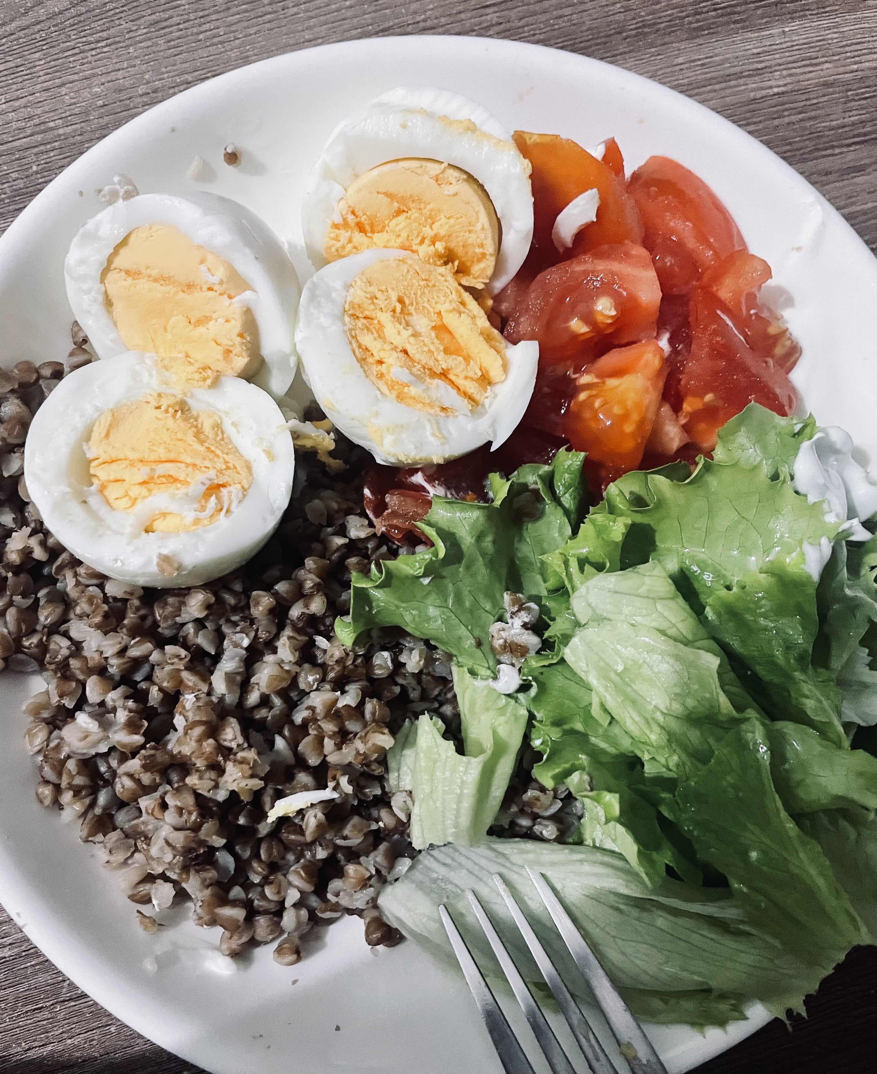 A balanced meal consisting of boiled eggs, buckwheat, fresh tomatoes, and lettuce, providing a good mix of protein, carbs, and fats.