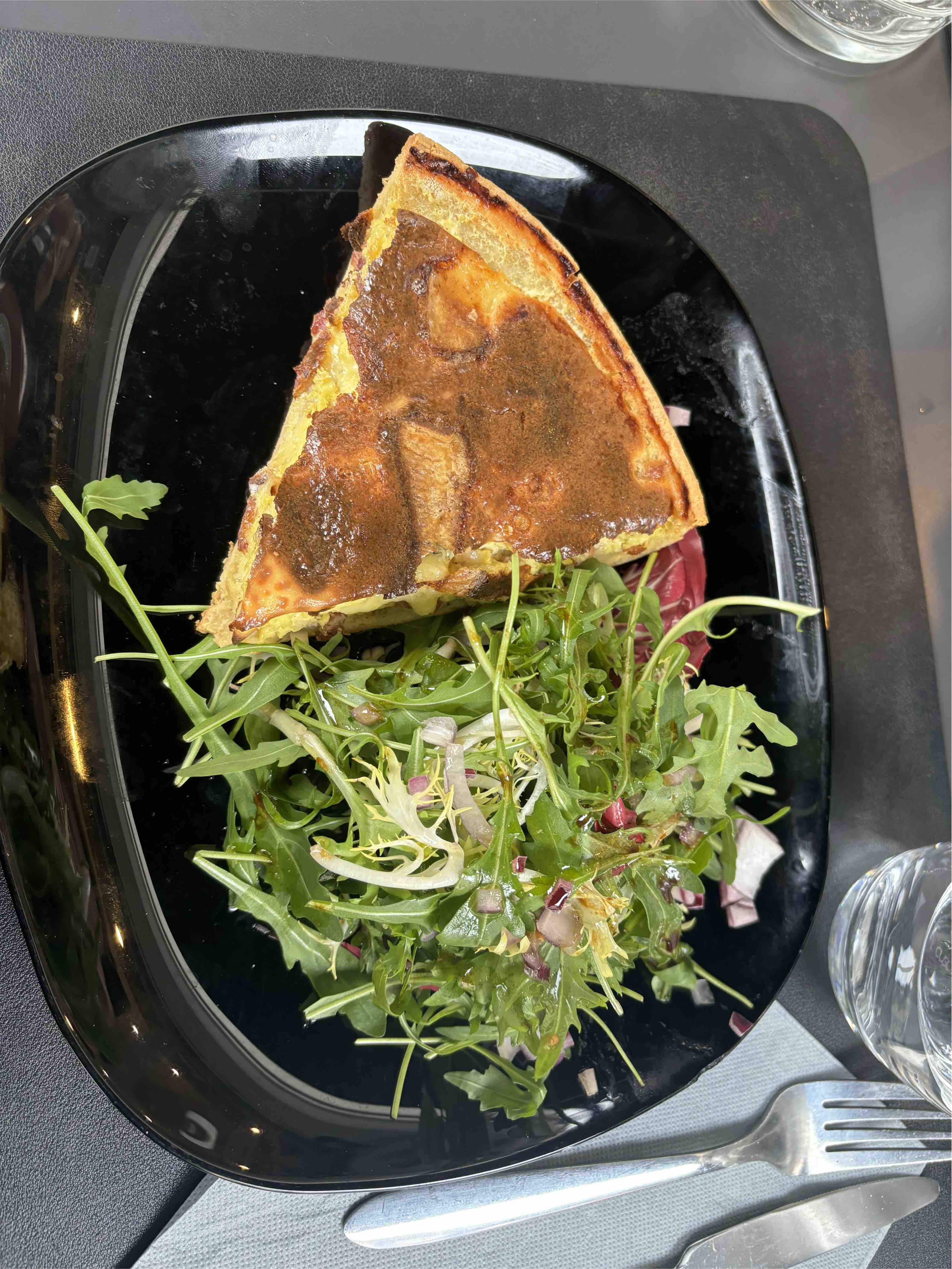 A slice of quiche served with a fresh arugula salad, garnished with onions and a light dressing.