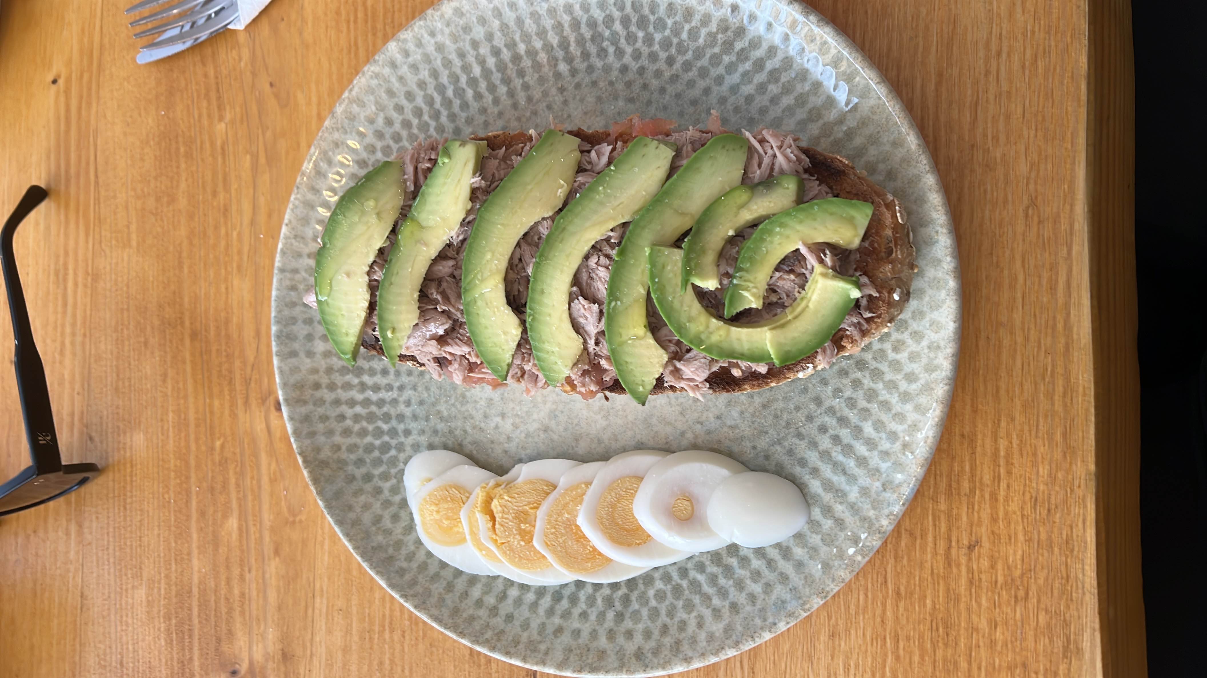 A nutritious meal consisting of avocado slices, tuna, and boiled egg served on whole grain bread.