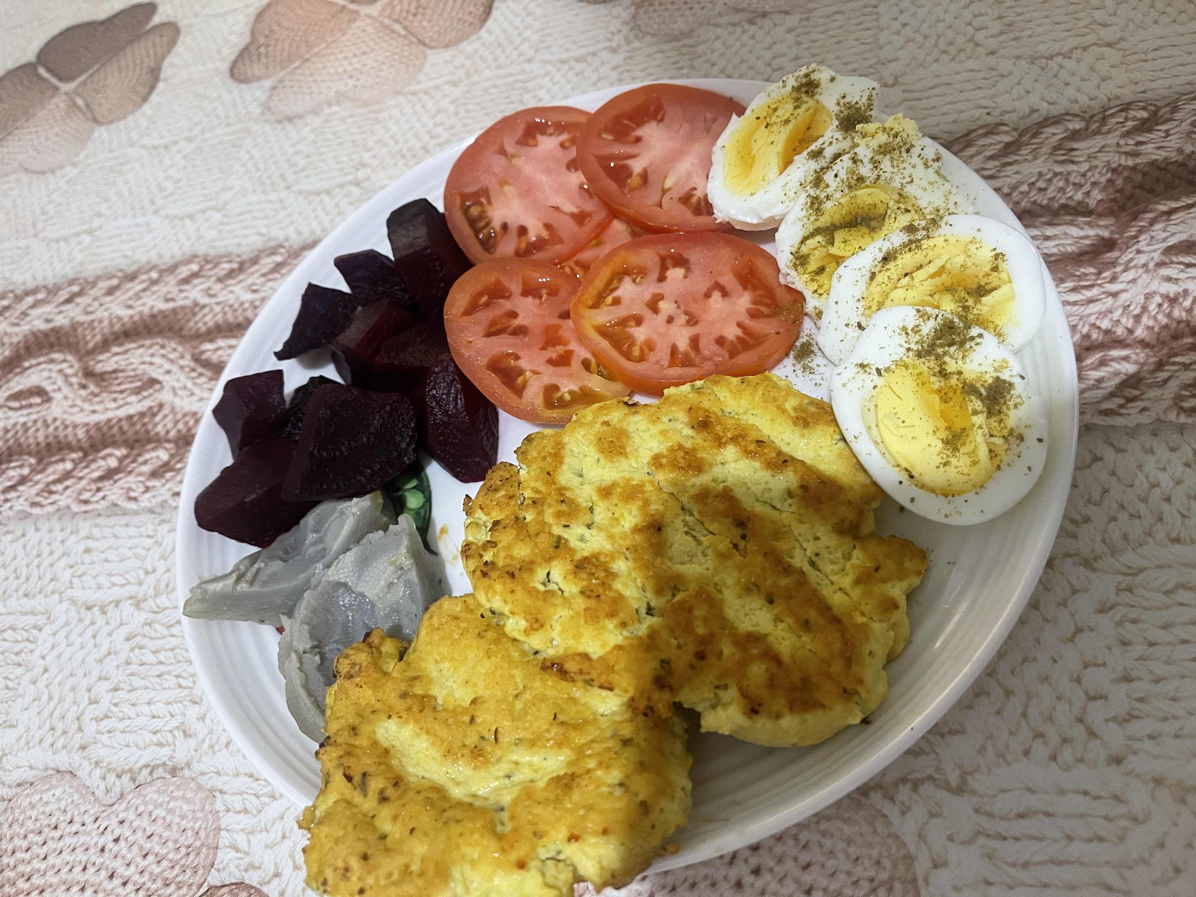 A balanced plate containing boiled eggs, tomato slices, beetroot, omelette, and artichoke, providing a mix of protein, carbs, and fats.