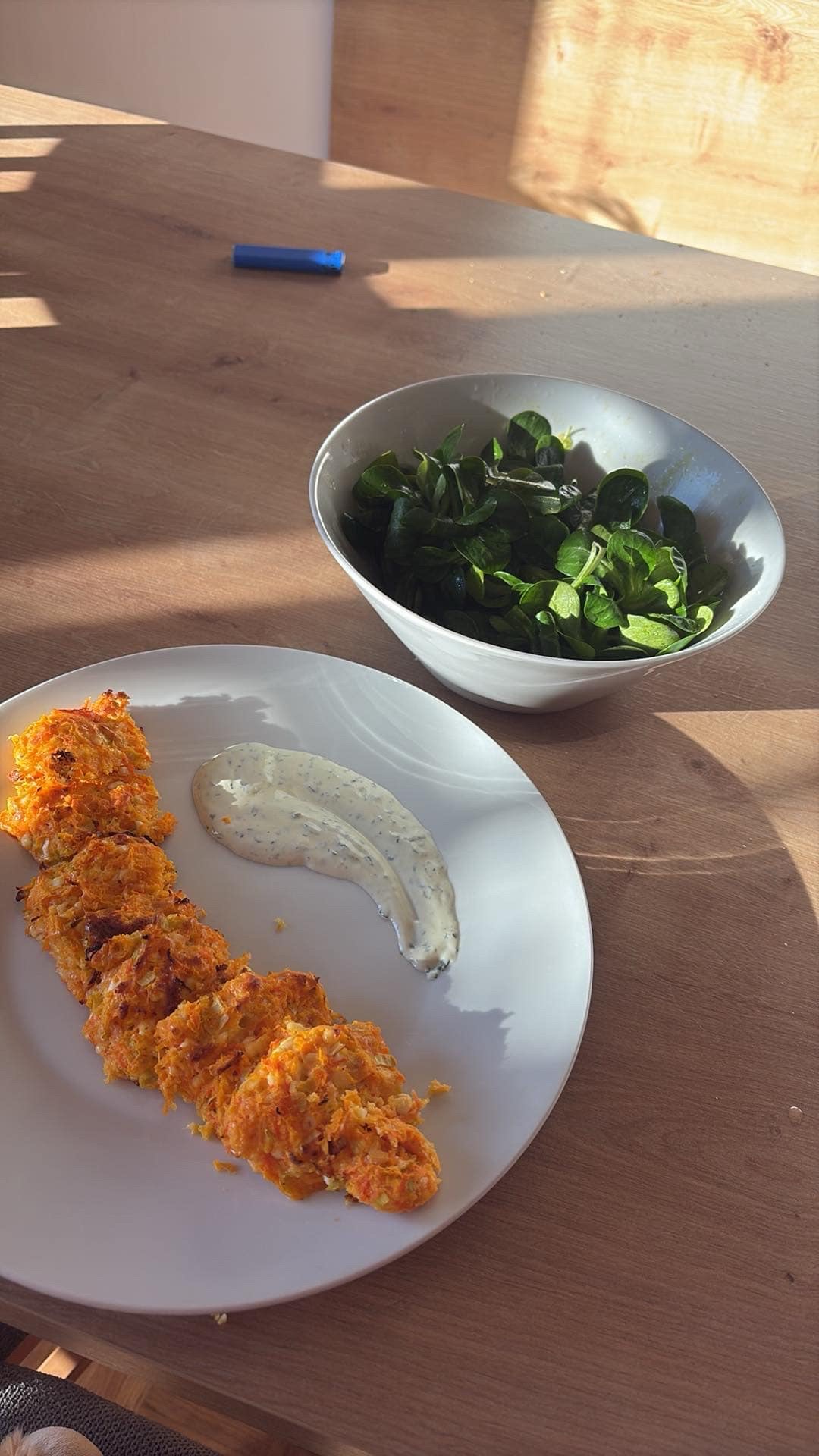 A plate of carrot fritters served with a creamy herb sauce and a side of fresh green salad.