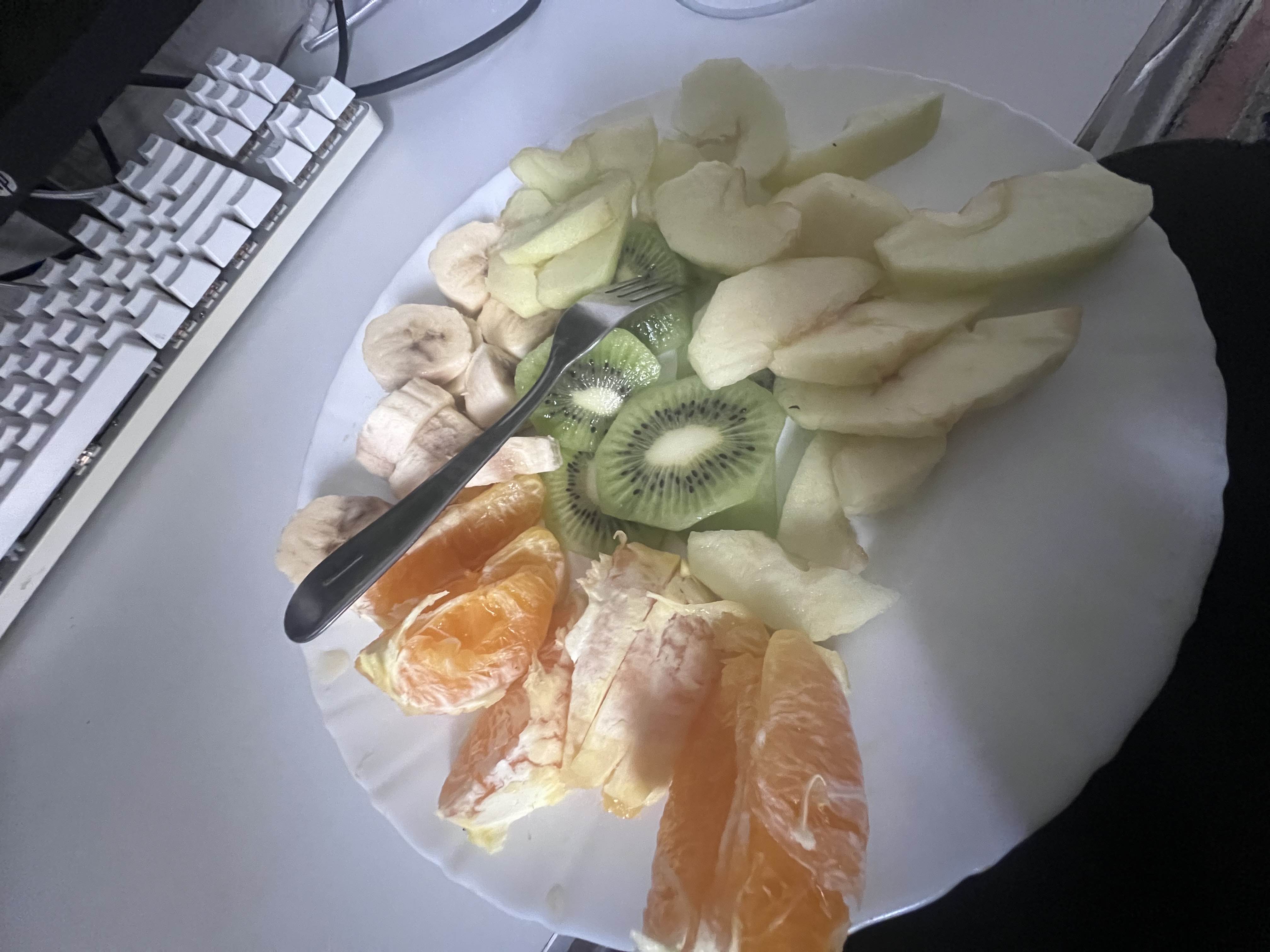 A plate of fresh fruits including orange slices, banana slices, kiwi slices, and apple slices, providing a healthy and nutrient-rich snack.