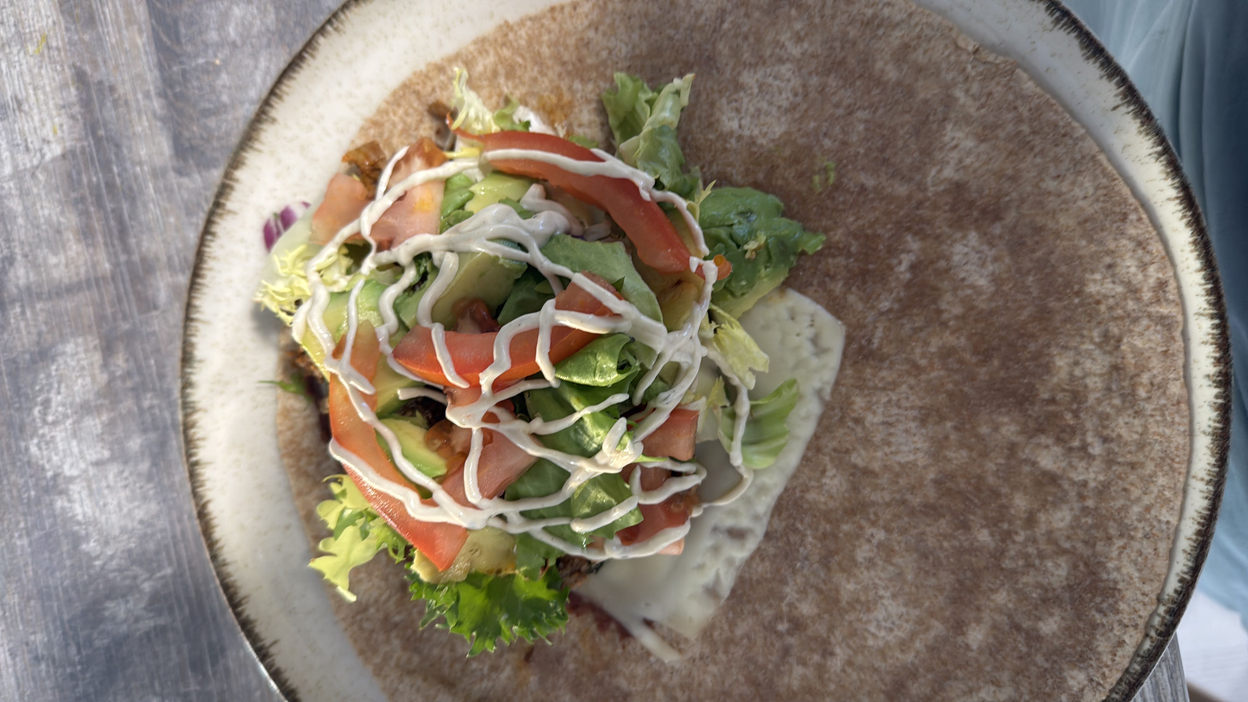 A healthy wrap containing fresh vegetables, avocado, cheese, and ranch dressing on a whole wheat base.