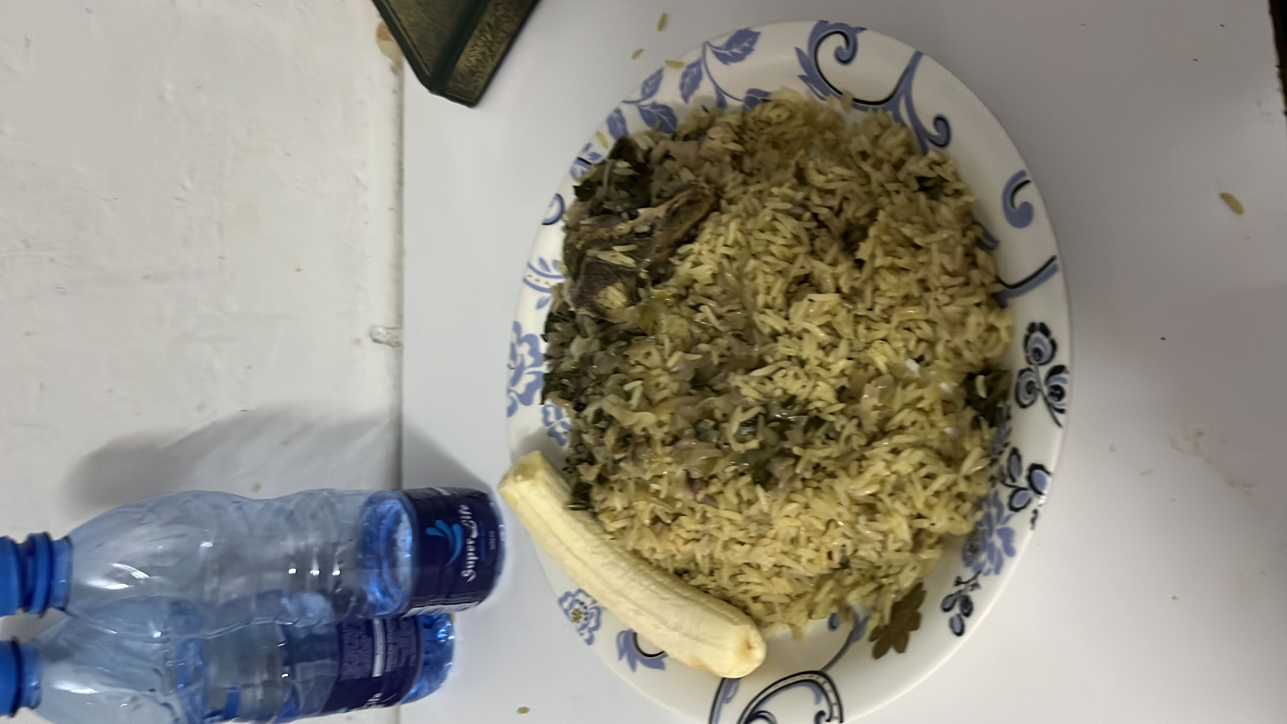 A plate of rice mixed with greens, a piece of meat, and a banana on the side, providing a balanced meal with moderate calories and nutrients.