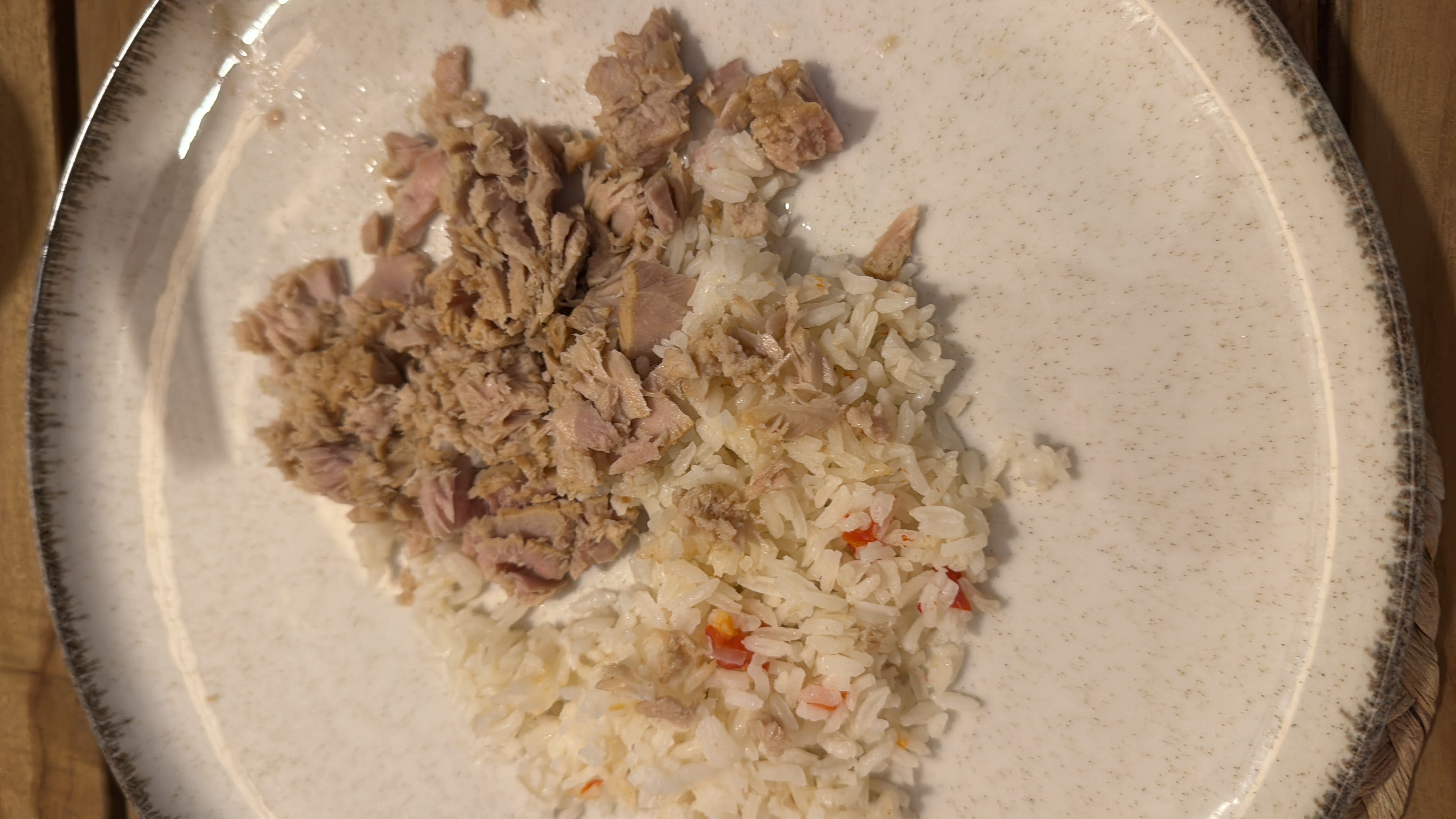 A plate containing cooked rice with small pieces of red pepper and shredded tuna, providing a balanced mix of protein and carbohydrates.