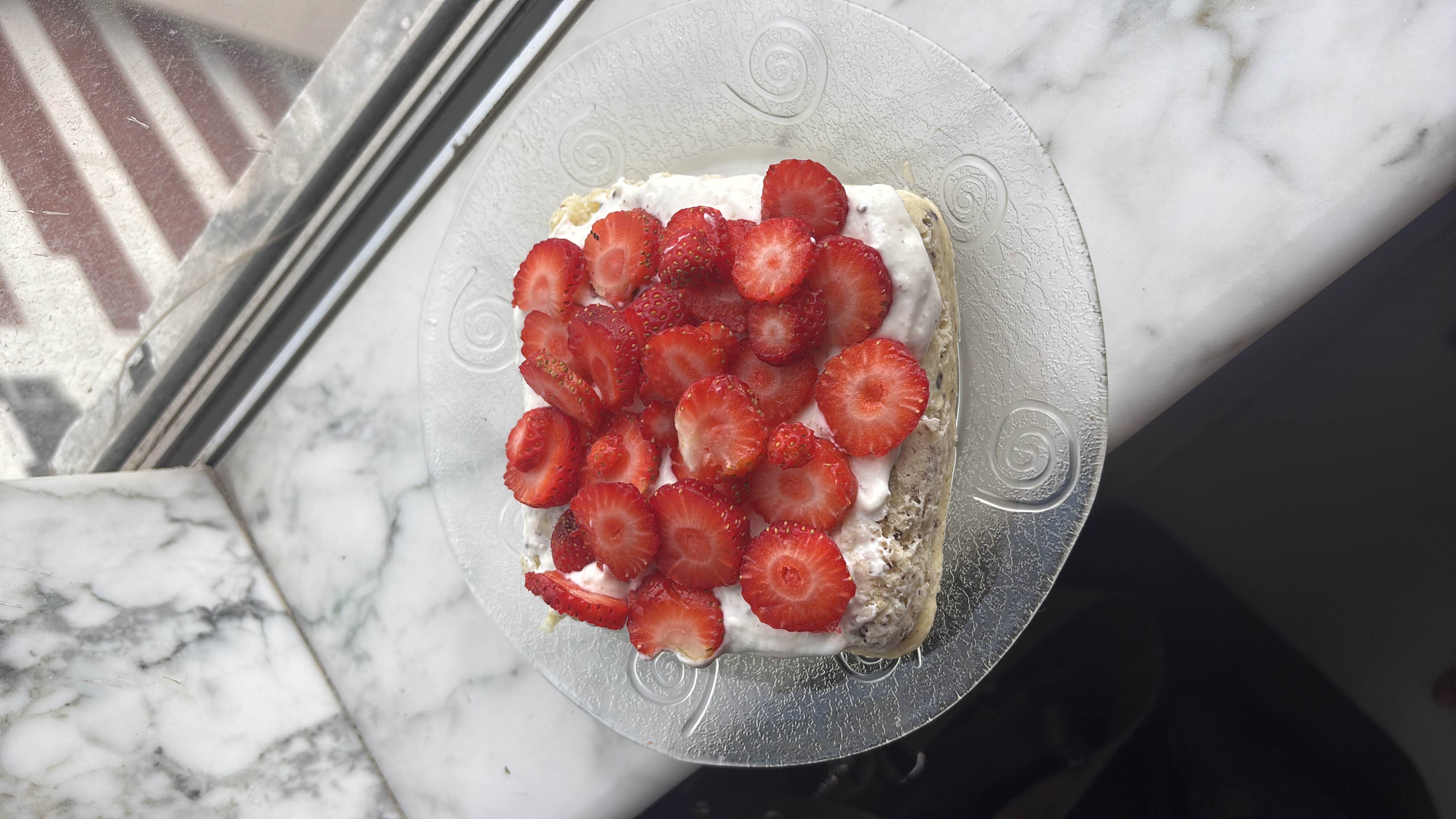 A nutritious dessert featuring a slice of banana bread topped with yogurt and fresh strawberries, enhanced with added protein for a balanced intake.