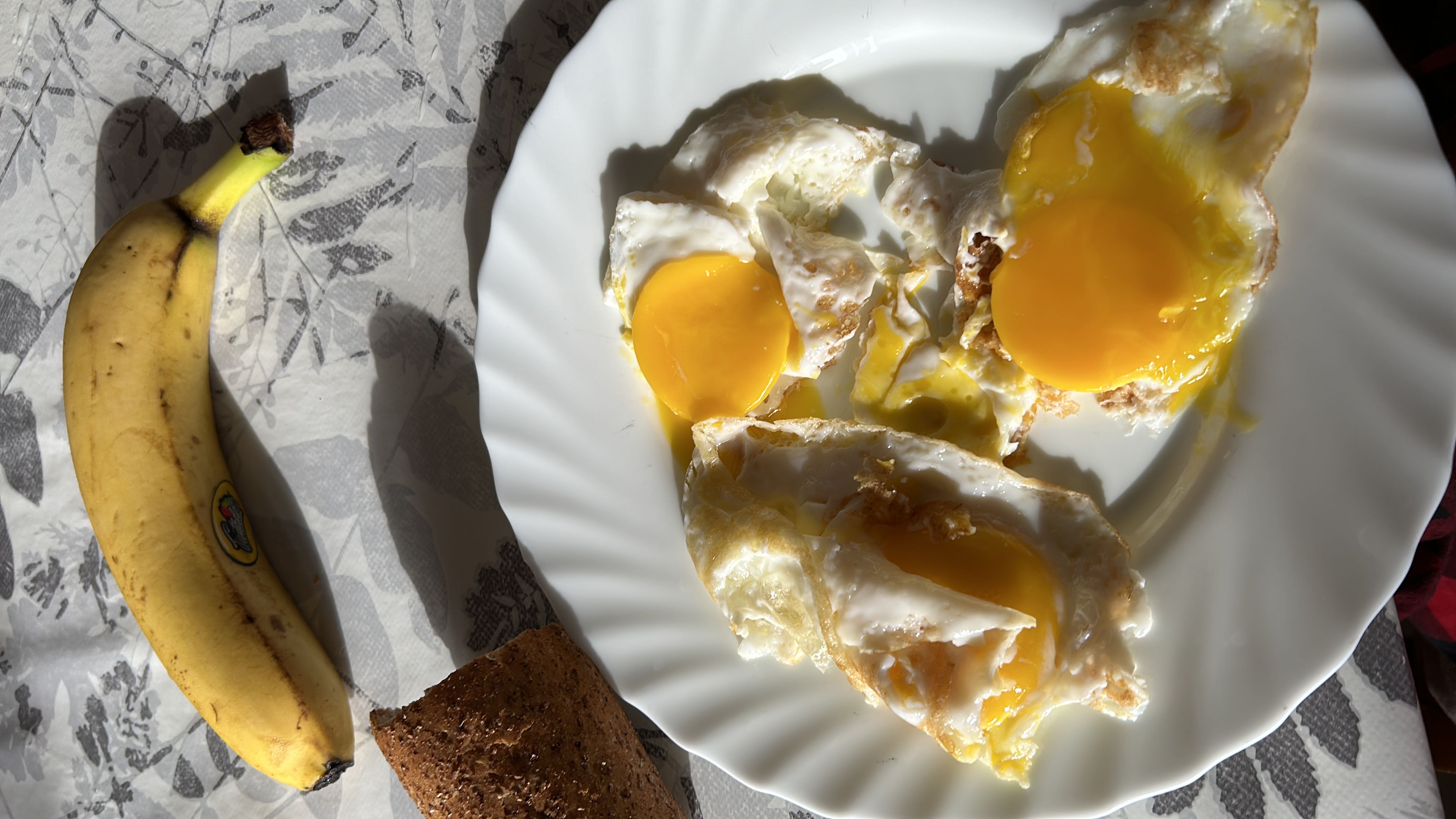 A balanced meal consisting of fried eggs, a banana, and a piece of whole grain bread, providing a good mix of protein, carbs, and fats.