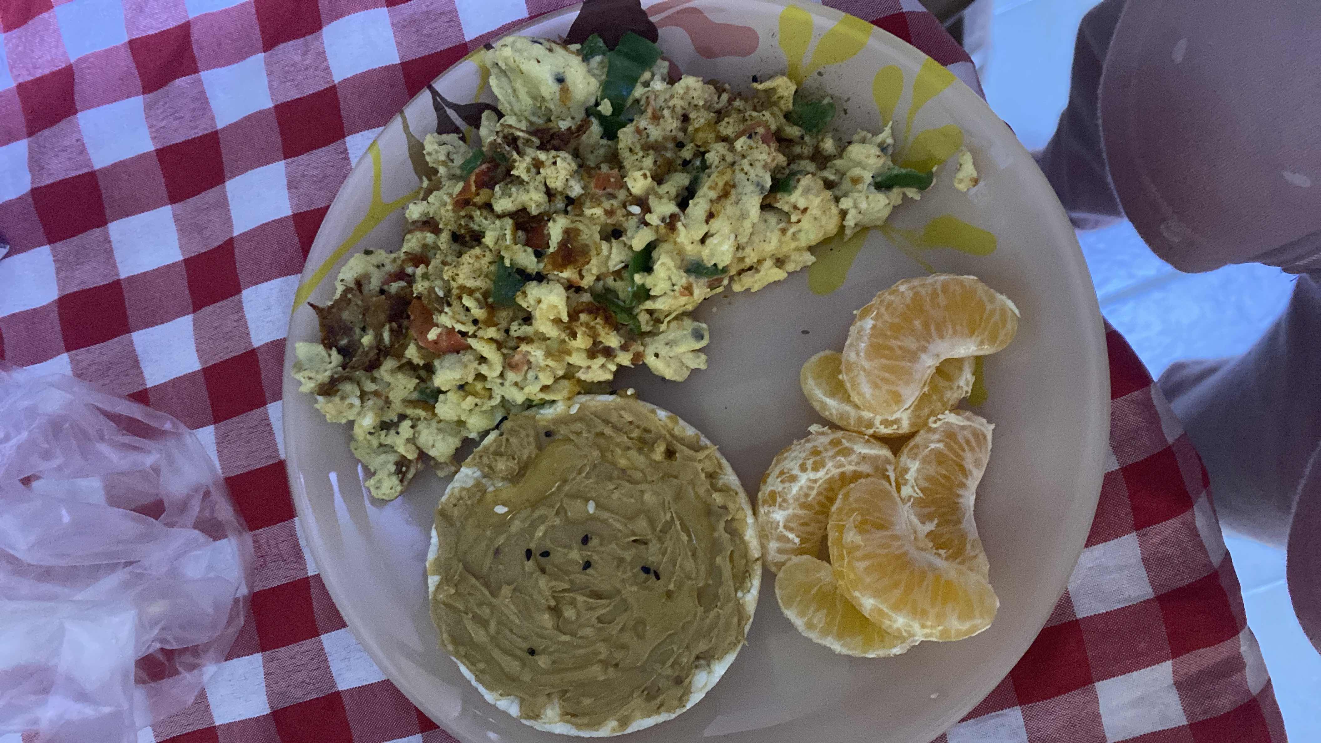 A balanced meal consisting of scrambled eggs with vegetables, a rice cake topped with peanut butter, and orange slices.