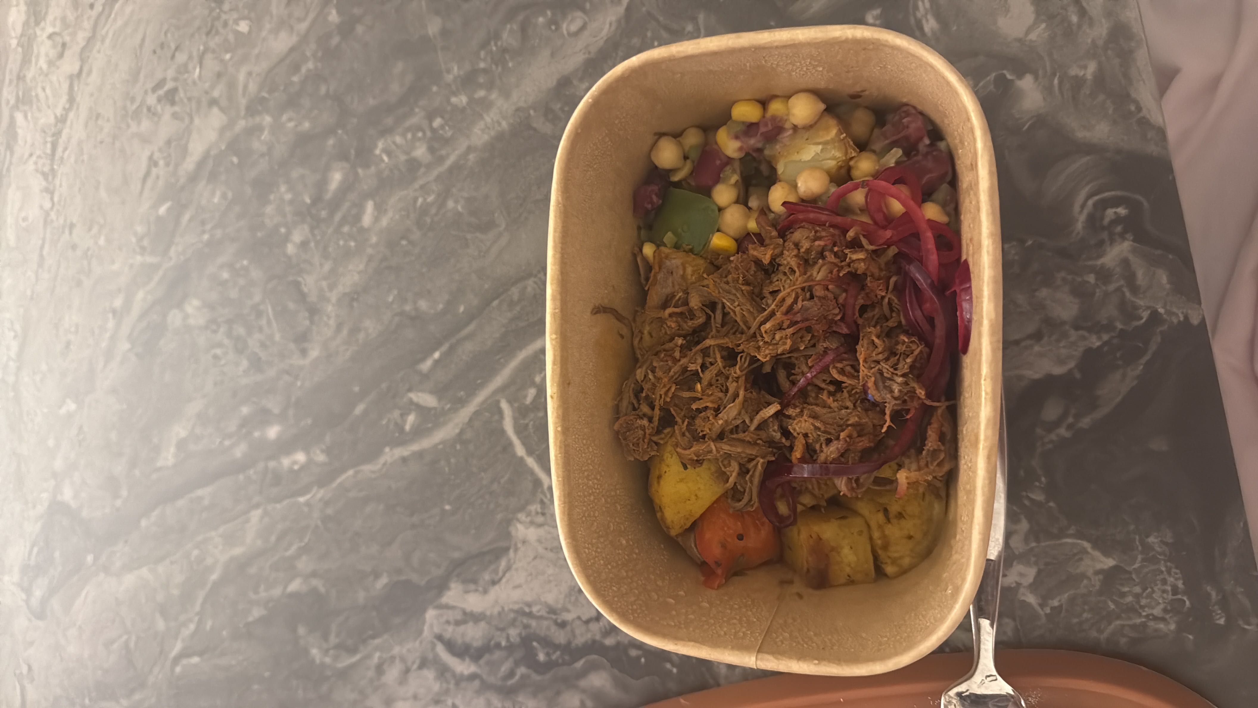 A balanced meal containing shredded beef, roasted potatoes, chickpeas, corn, and red onions, providing a good mix of protein, carbs, and fats.