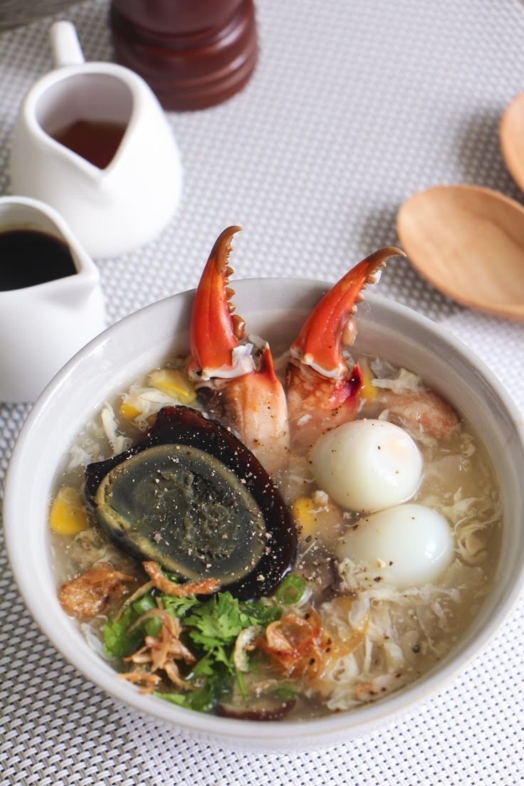 A hearty soup featuring crab claws, century egg, quail eggs, and garnished with fried shallots and cilantro, served in a flavorful broth.