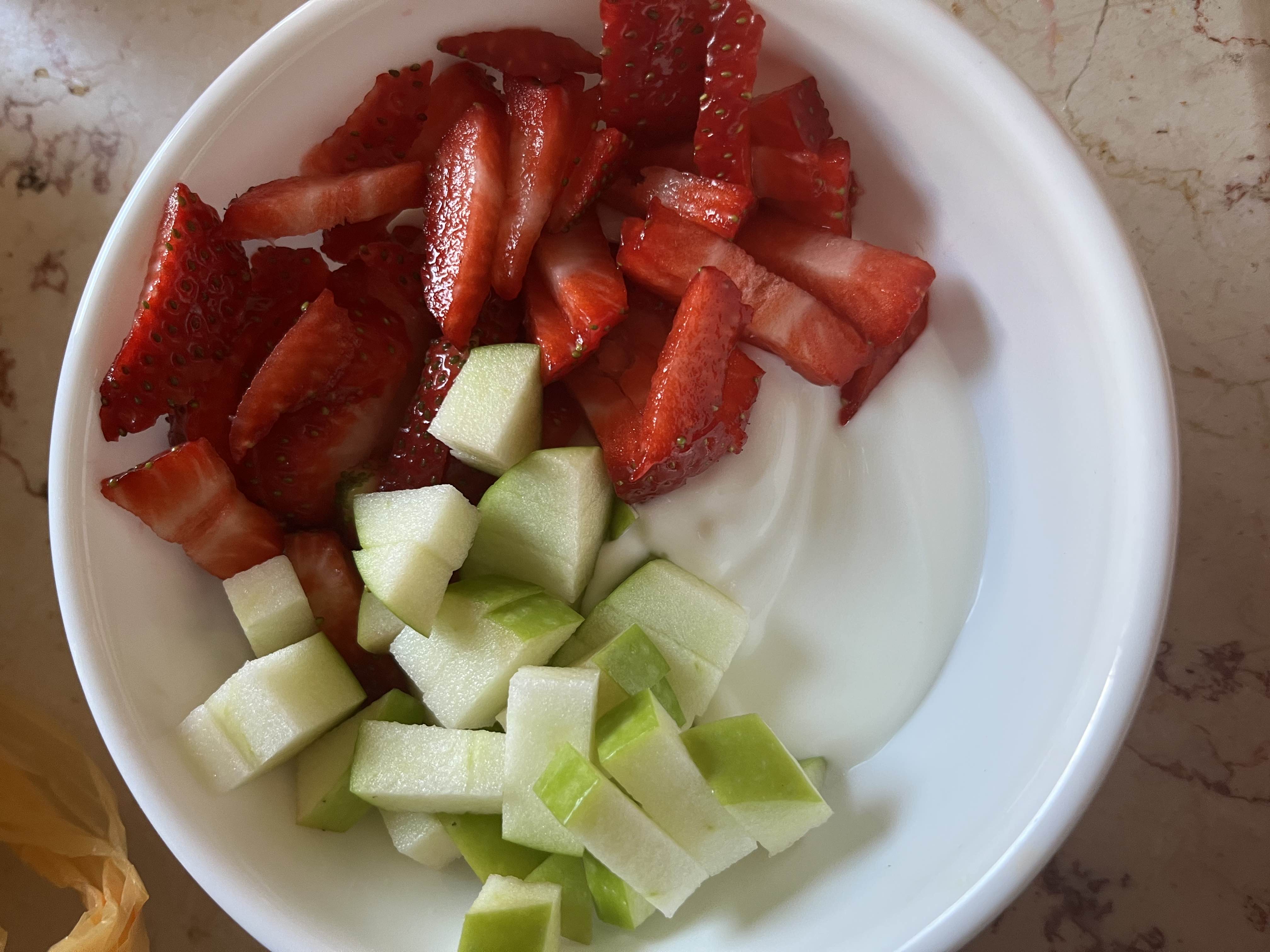 A healthy bowl containing yogurt topped with fresh strawberries and green apple slices, providing a balanced mix of protein, carbs, and fats.