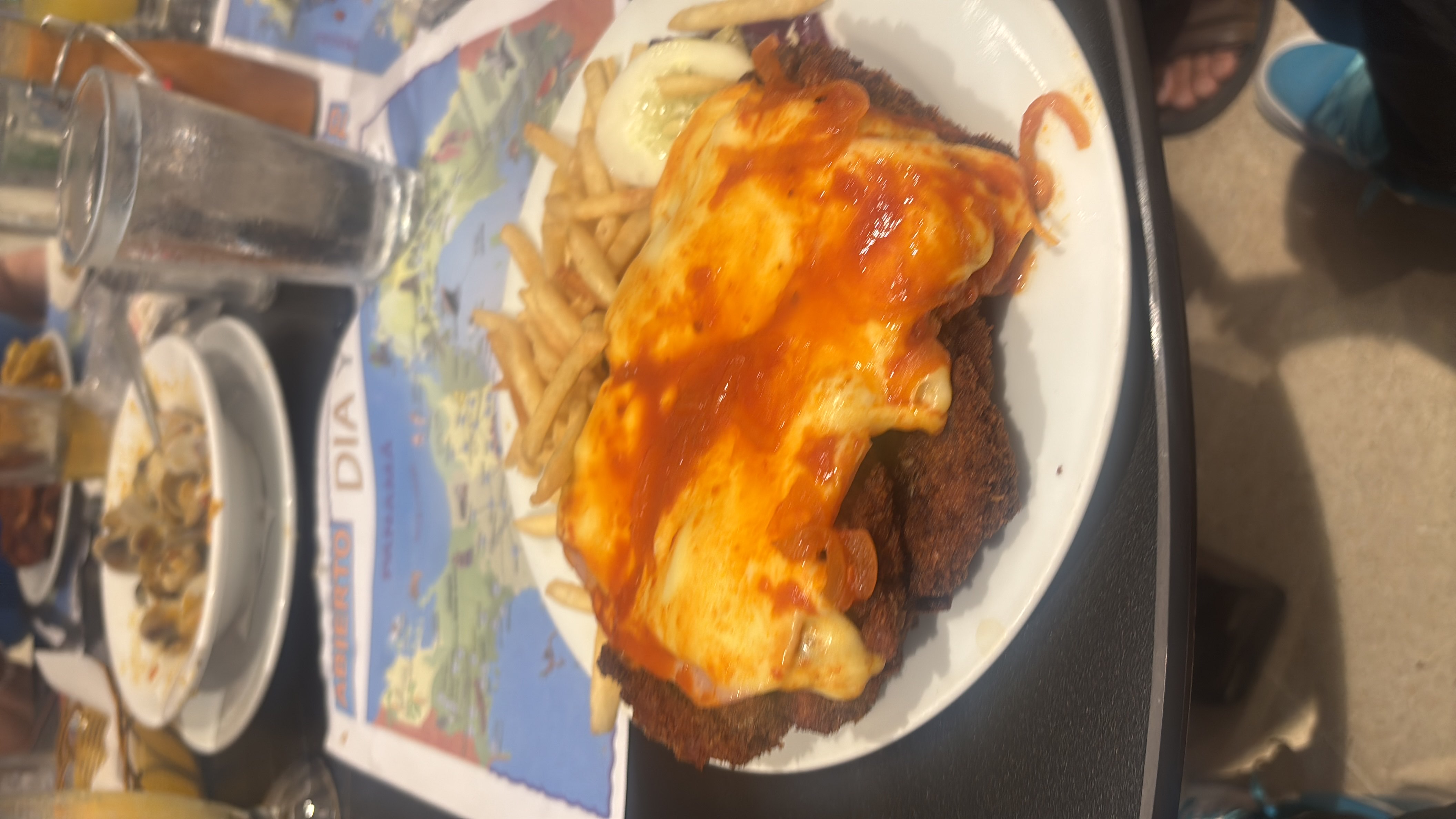 A plate of breaded chicken topped with melted cheese and tomato sauce, served with a side of french fries and a cucumber slice.