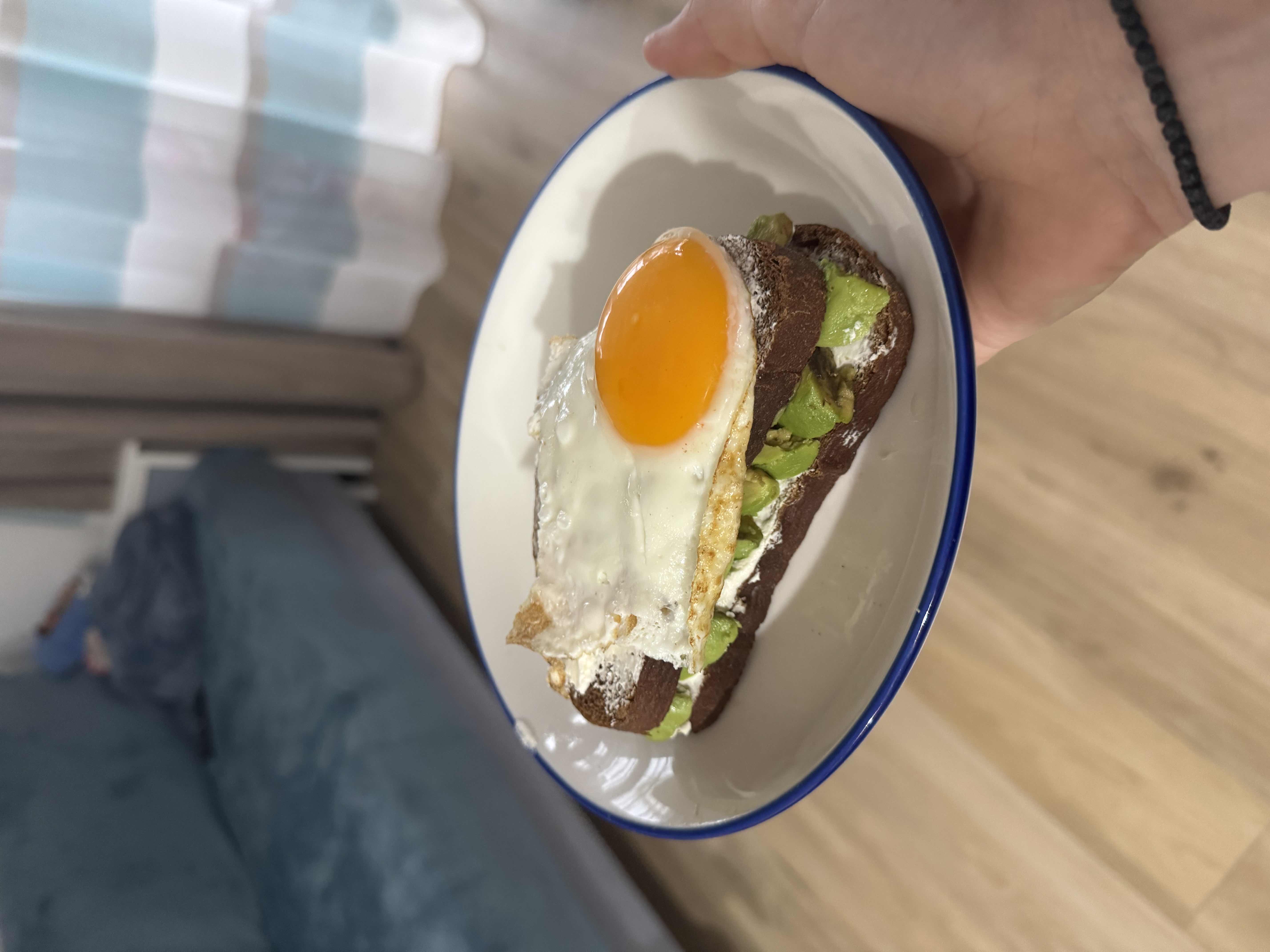 A nutritious open-faced sandwich with whole-grain bread, avocado slices, cream cheese, and a fried egg on top.