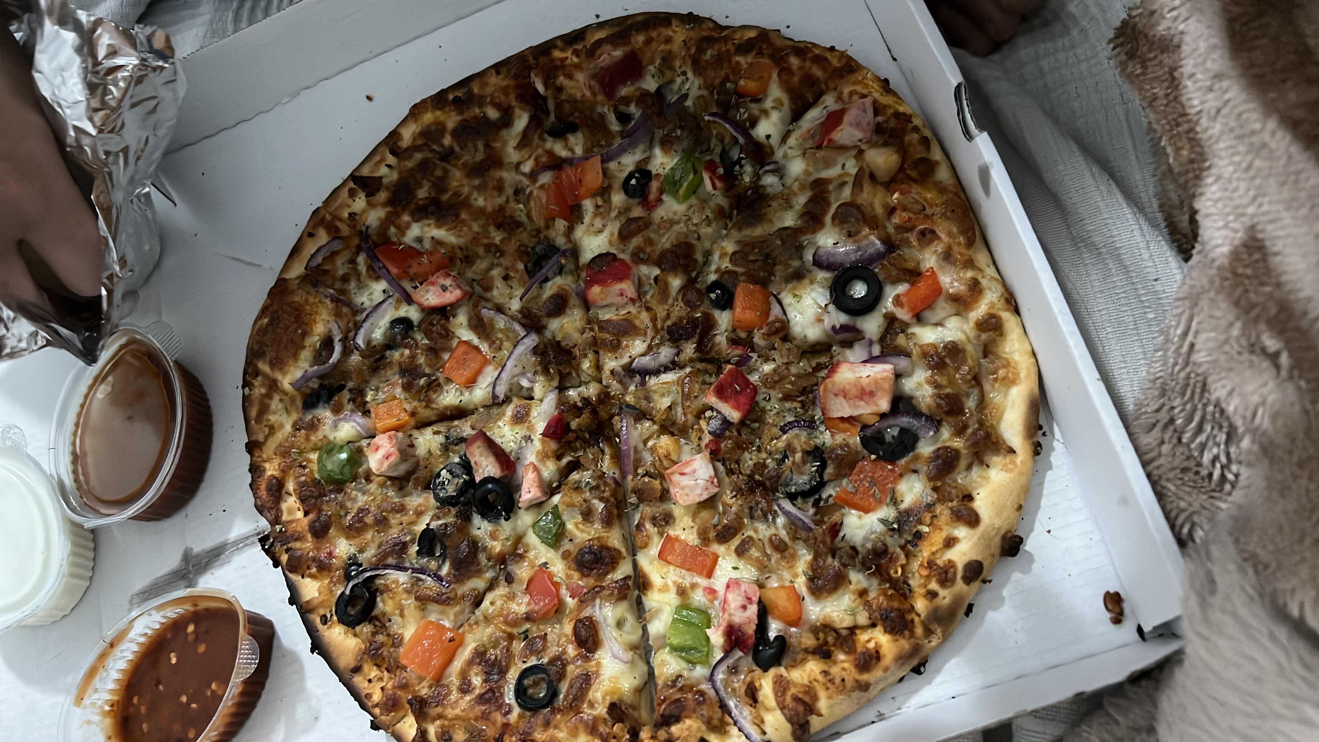 A pizza topped with cheese, vegetables, olives, and meat, served with dipping sauces.