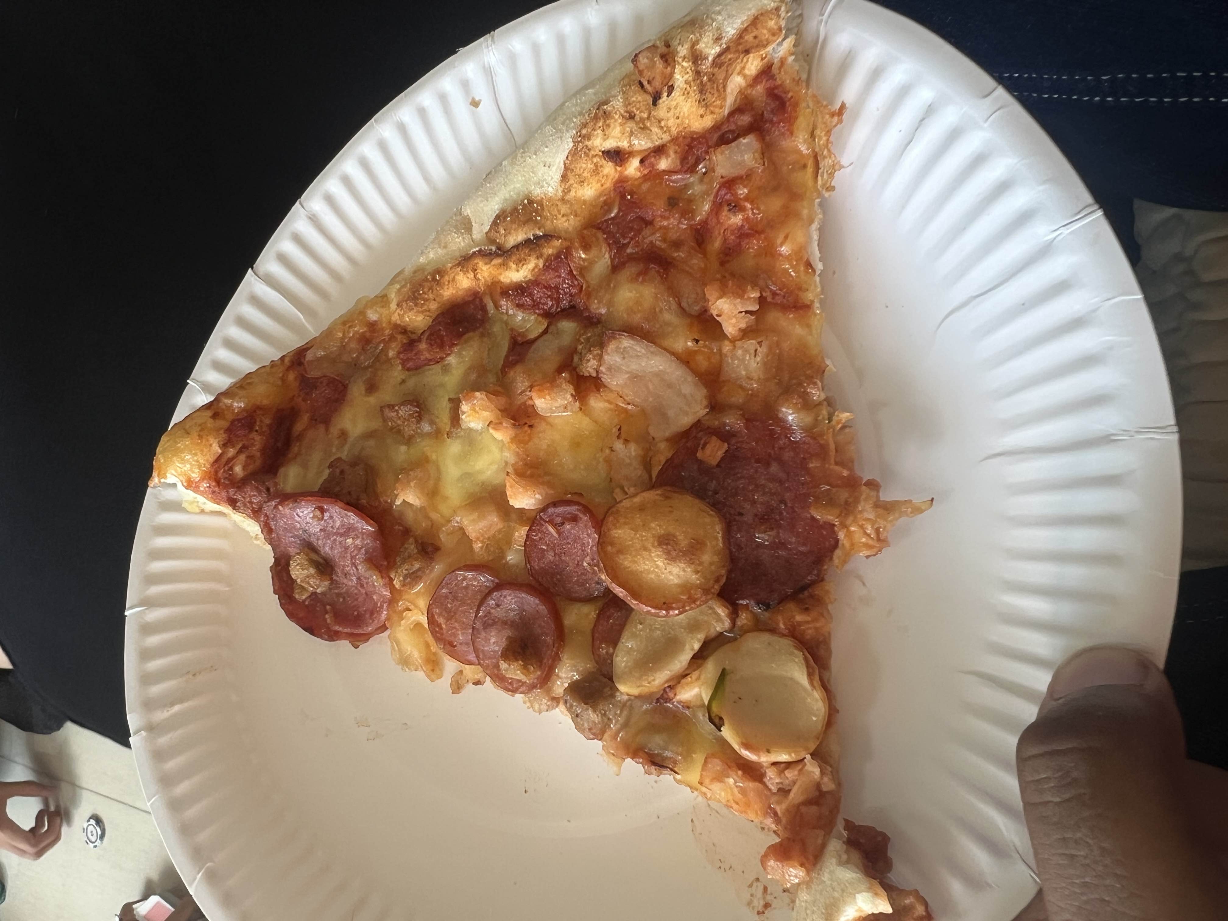 A slice of pepperoni pizza with cheese, tomato sauce, a thin crust, and chicken chunks, served on a paper plate.