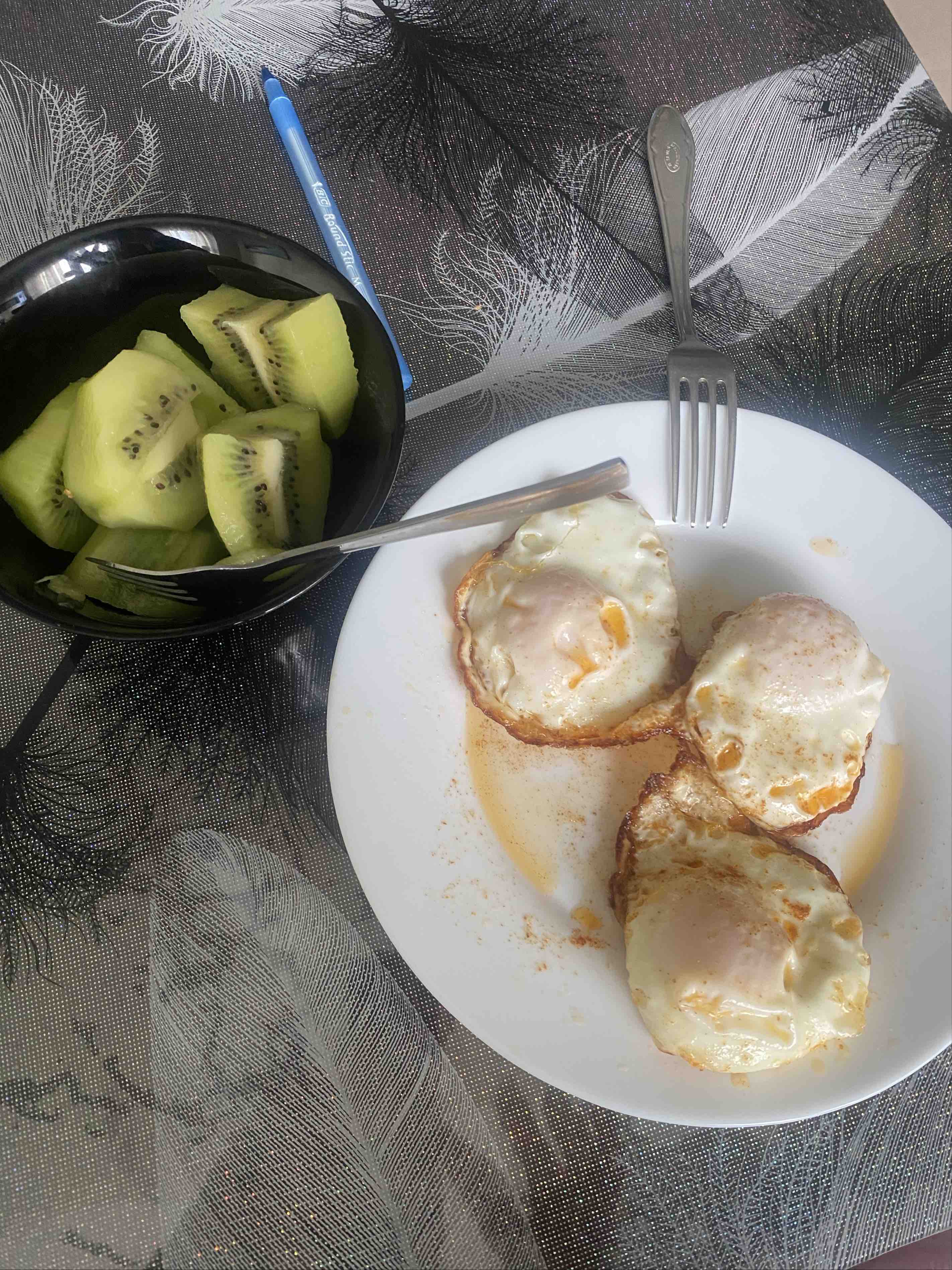 The image shows a meal consisting of three fried eggs and a bowl of sliced kiwi, providing a balanced mix of protein, healthy fats, and carbohydrates.