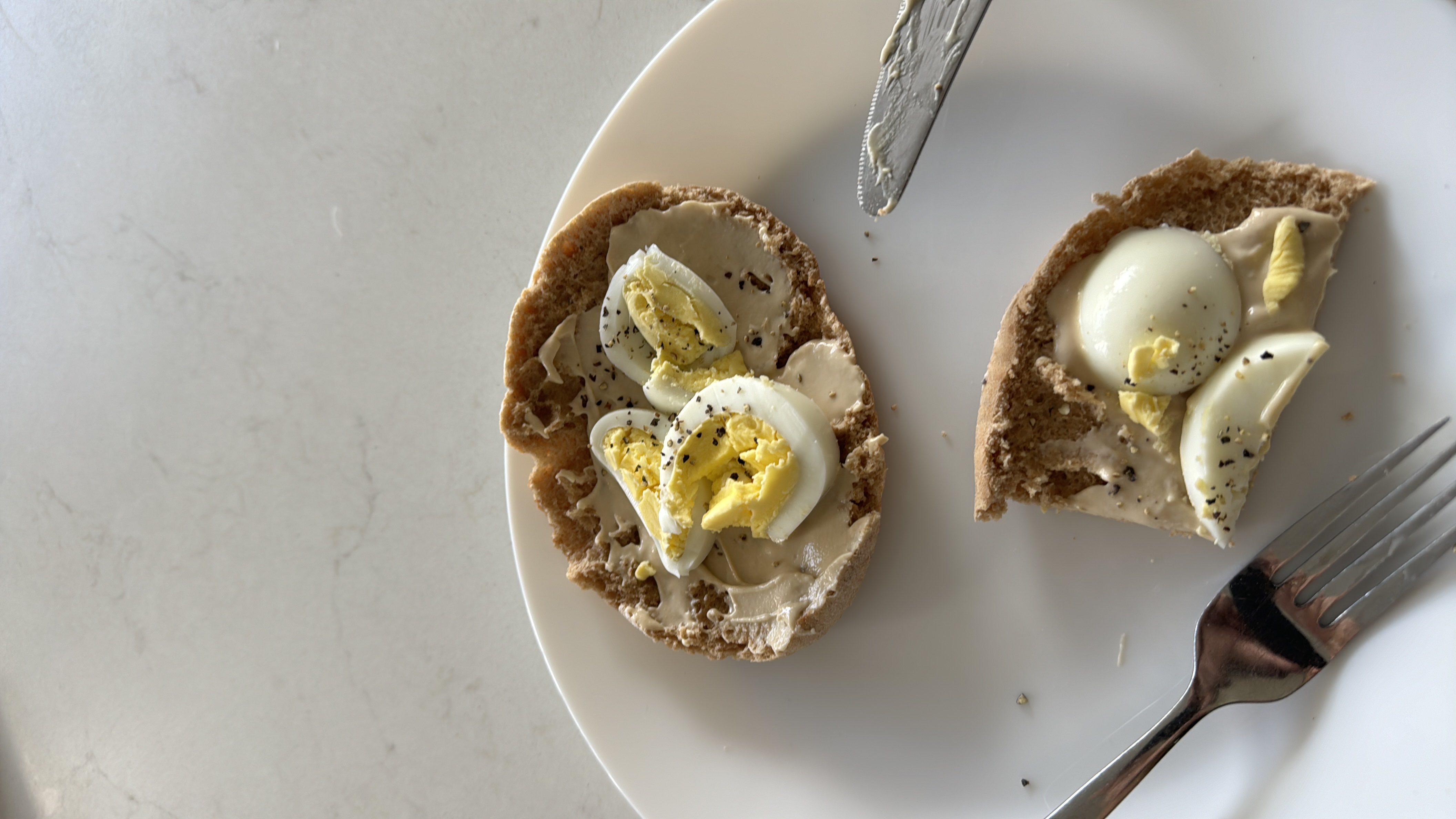 A nutritious snack consisting of whole grain bread topped with hummus and slices of boiled egg, seasoned with black pepper.
