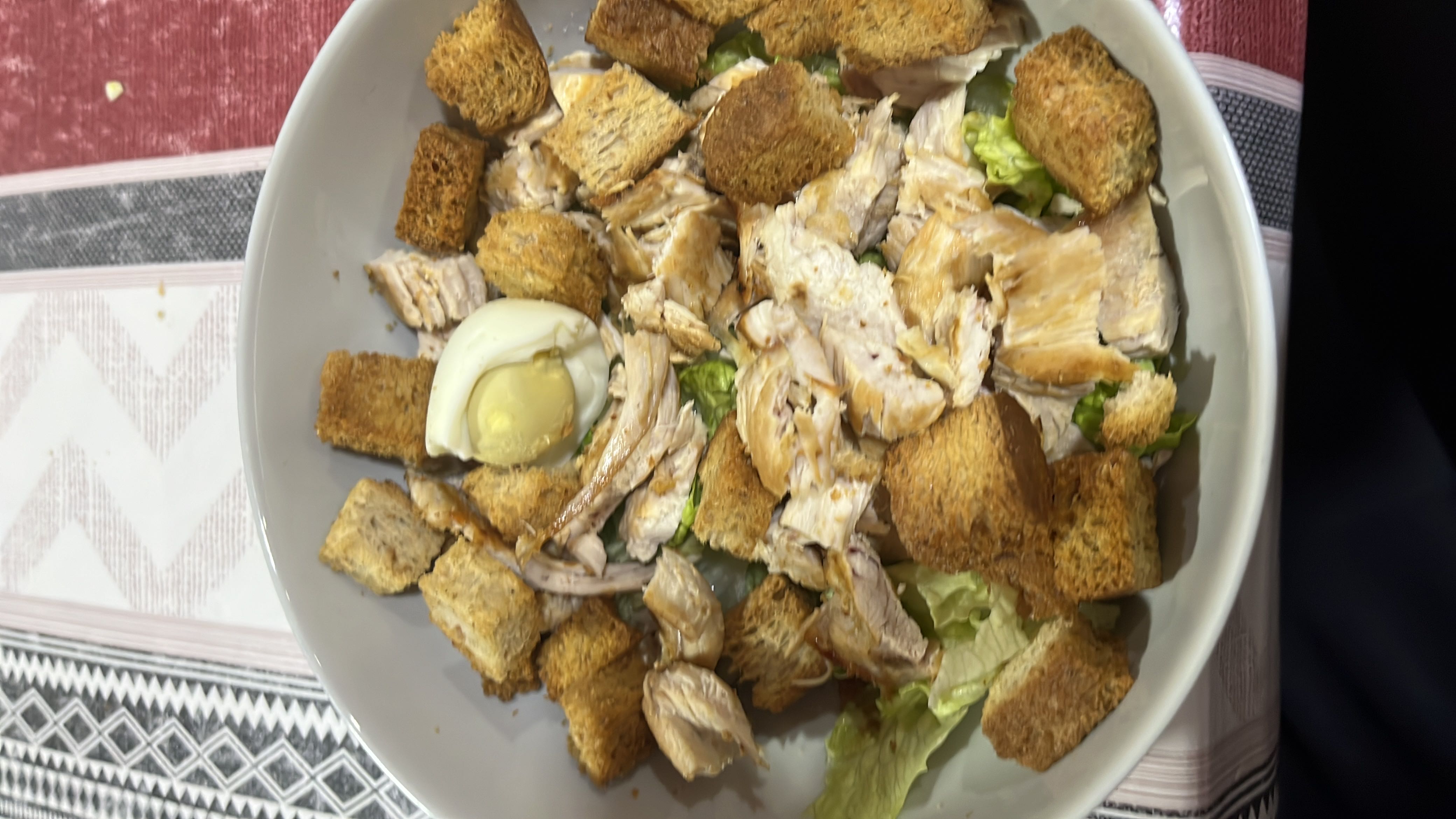 A Caesar salad with grilled chicken, croutons, lettuce, and a boiled egg, providing a balanced mix of protein, carbs, and fats.