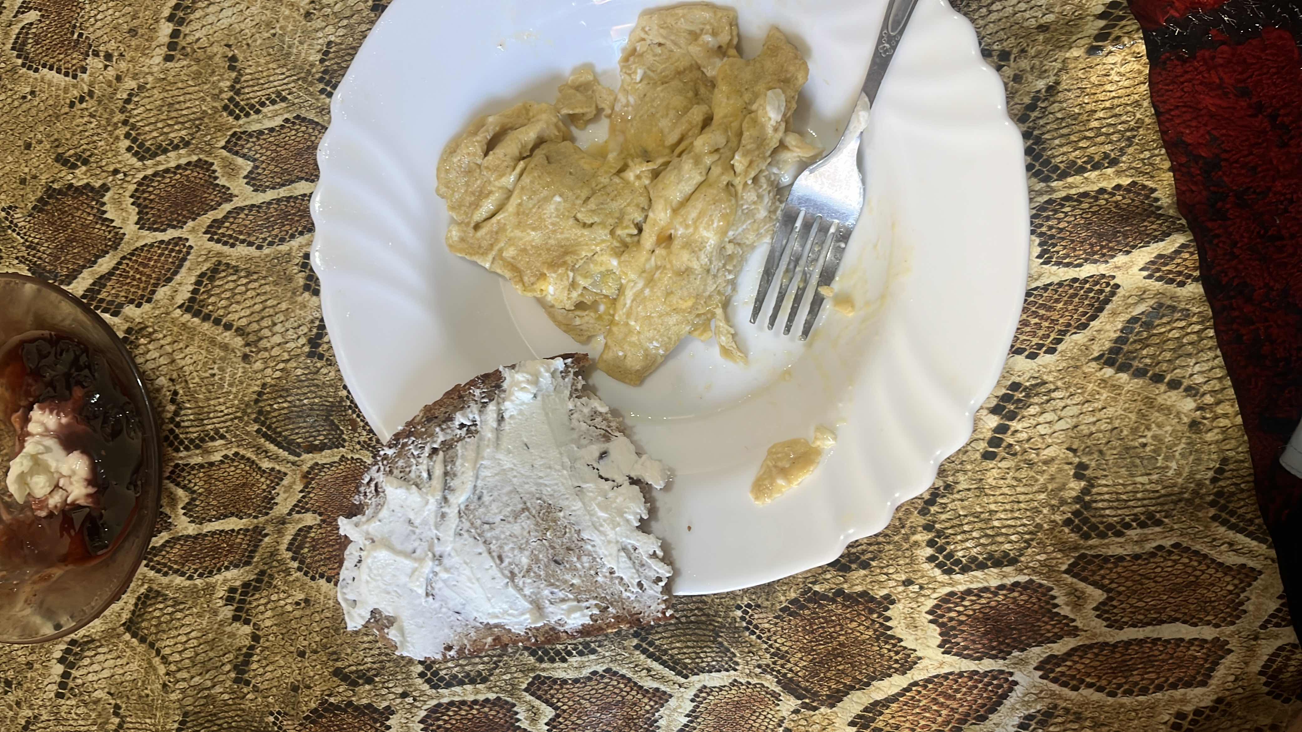 A meal consisting of scrambled eggs, bread with cream cheese, and a side of jam.