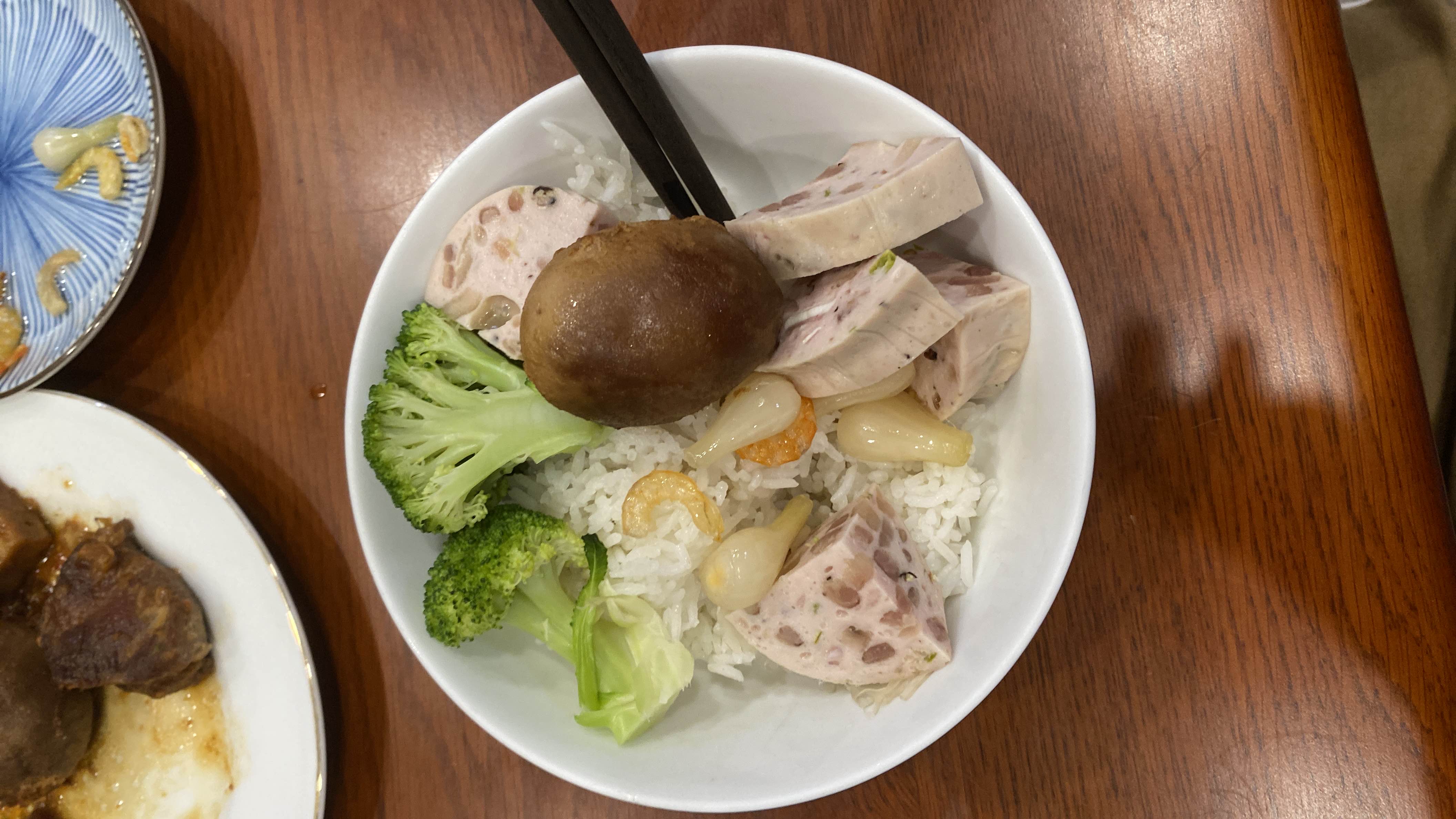 A balanced meal consisting of rice, broccoli, mushroom, lotus root sausage, and pickled garlic, providing a moderate calorie count and a good mix of macronutrients.