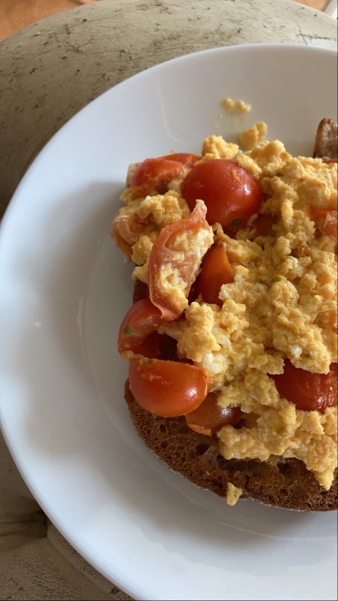 A nutritious dish consisting of scrambled eggs, cherry tomatoes, and whole-grain toast, providing a balanced mix of protein, carbs, and fats.