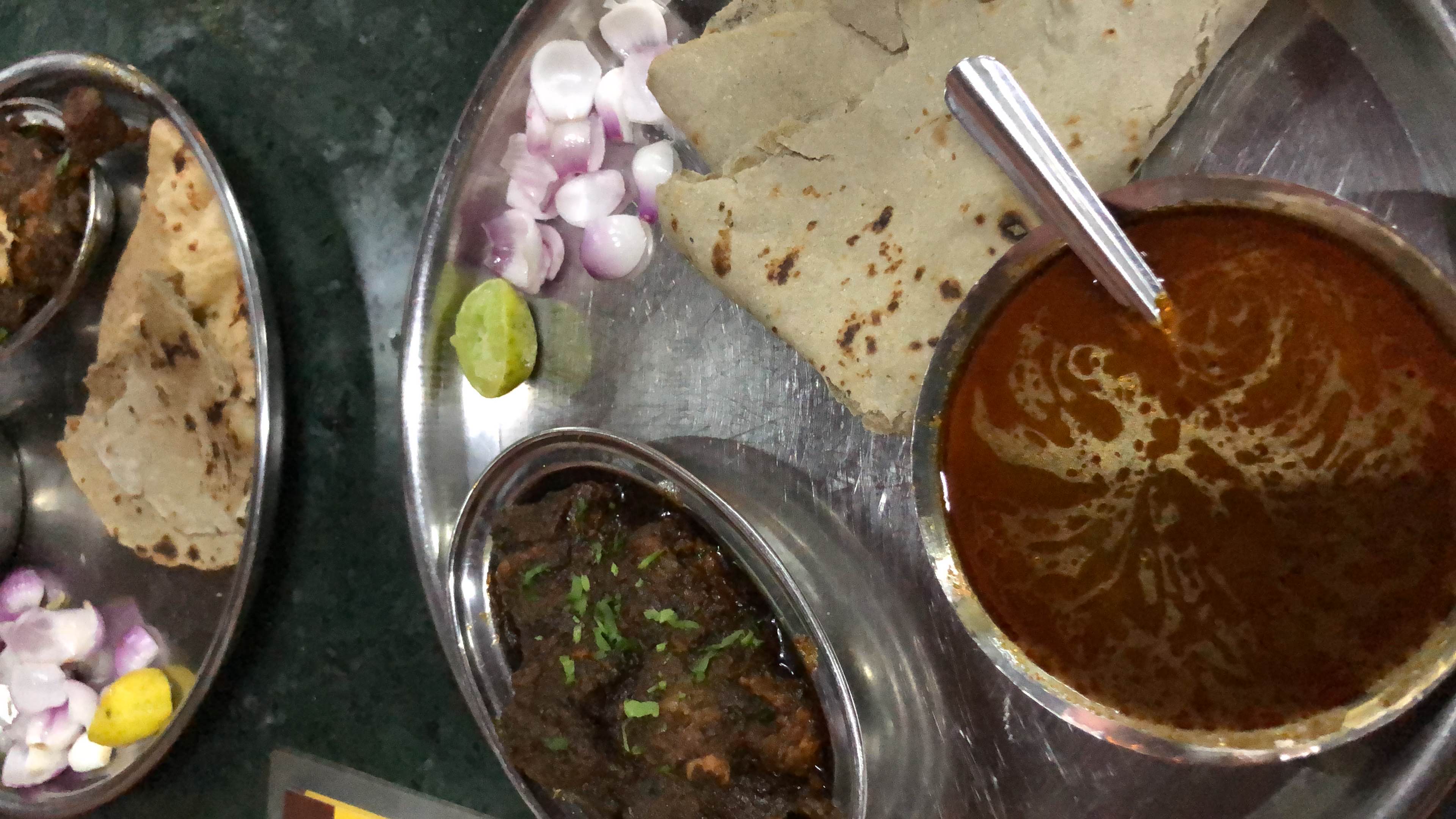 A traditional Indian meal consisting of chicken curry, roti, spicy gravy, onions, and lemon.