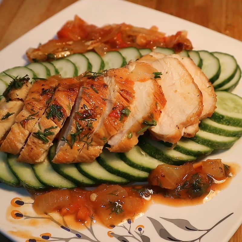 A healthy dish featuring grilled chicken breast served on a bed of fresh cucumber slices, garnished with herbs and accompanied by a light tomato-based sauce.