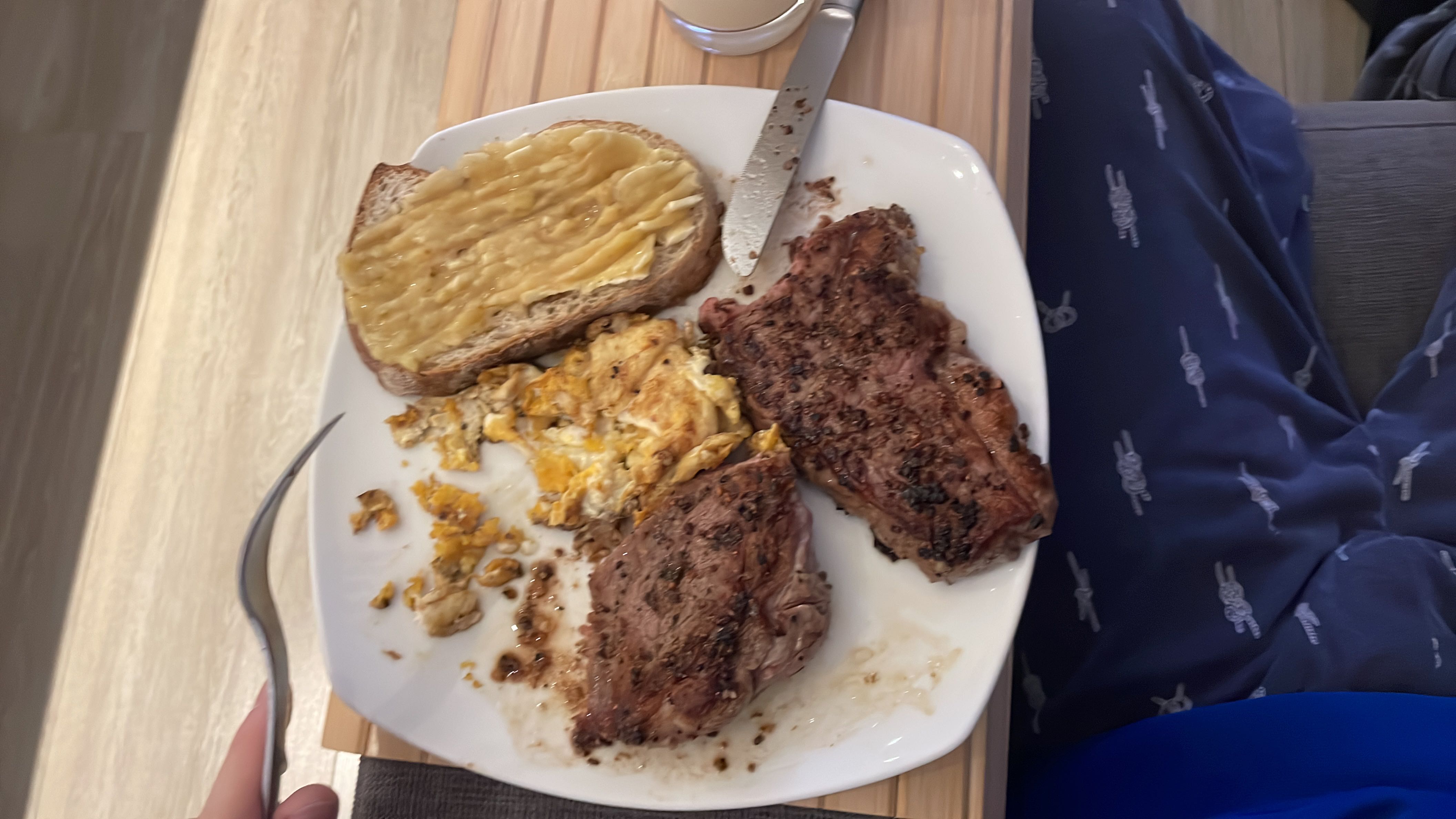 A meal consisting of two pieces of steak, scrambled eggs, and a slice of bread with peanut butter.