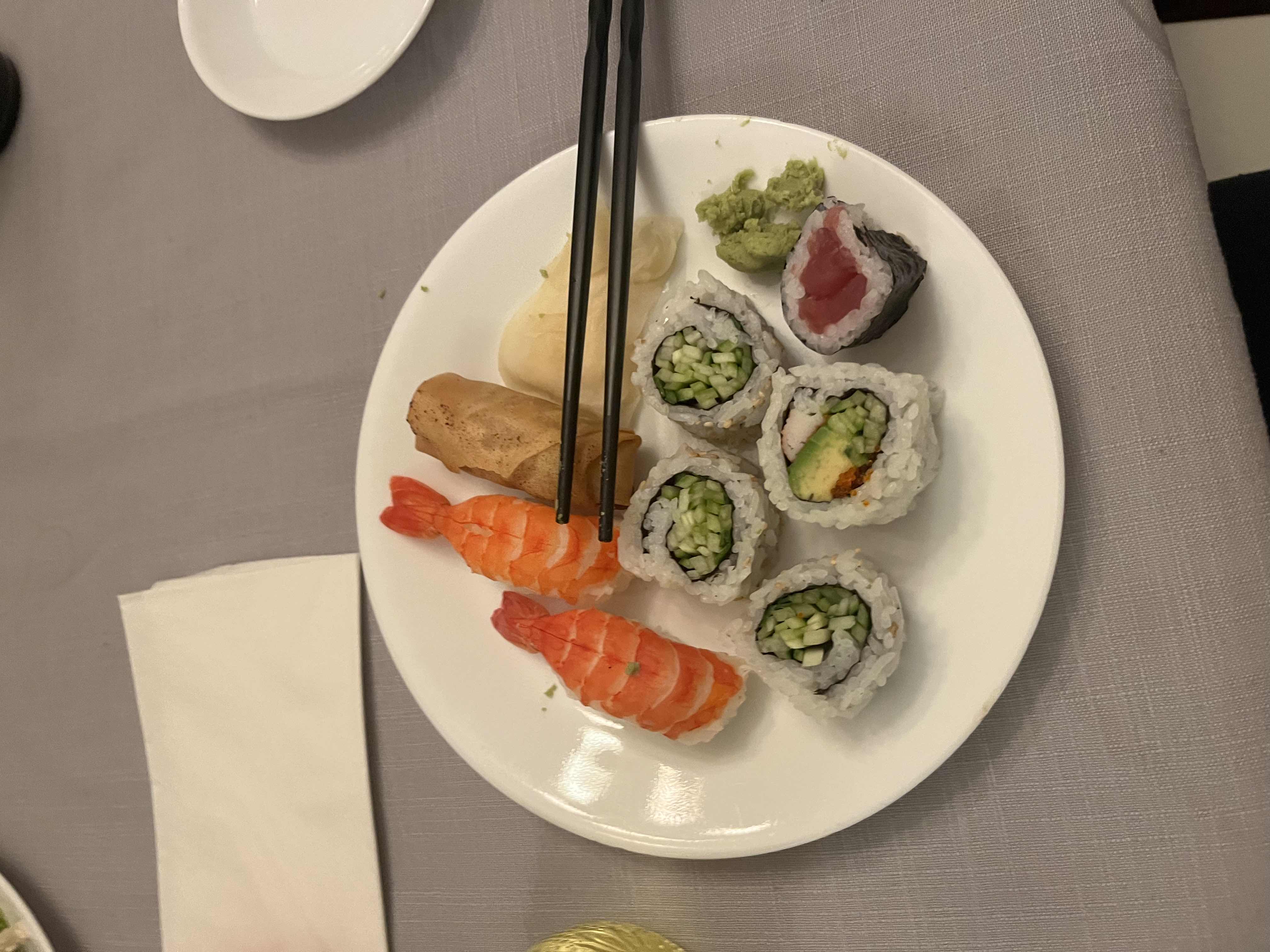 A plate of sushi including shrimp nigiri, cucumber rolls, avocado rolls, and tuna rolls, served with wasabi and pickled ginger.