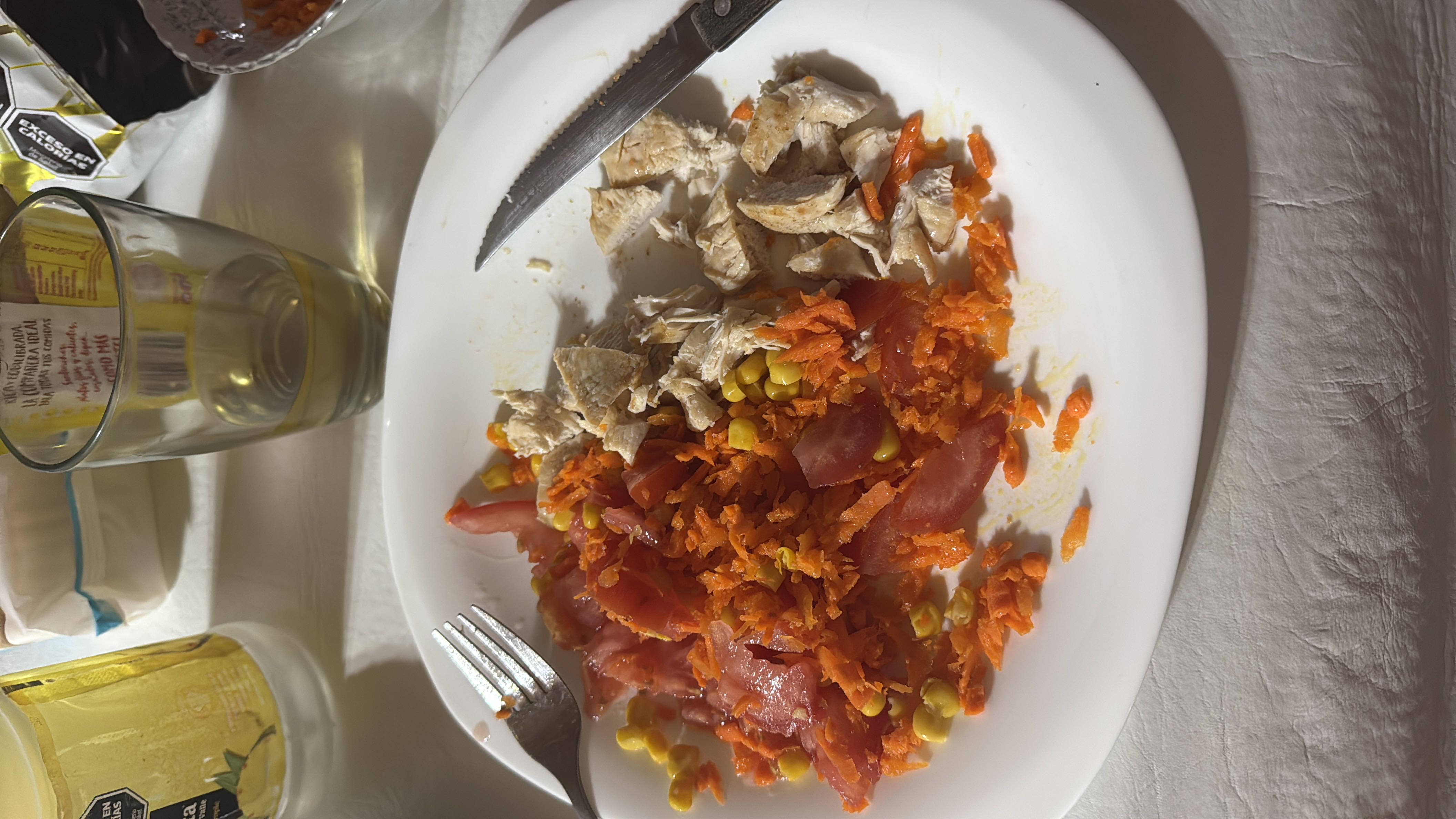 A healthy meal consisting of grilled chicken breast, shredded carrots, sliced tomatoes, and corn, providing a balanced mix of protein, carbs, and low fats.