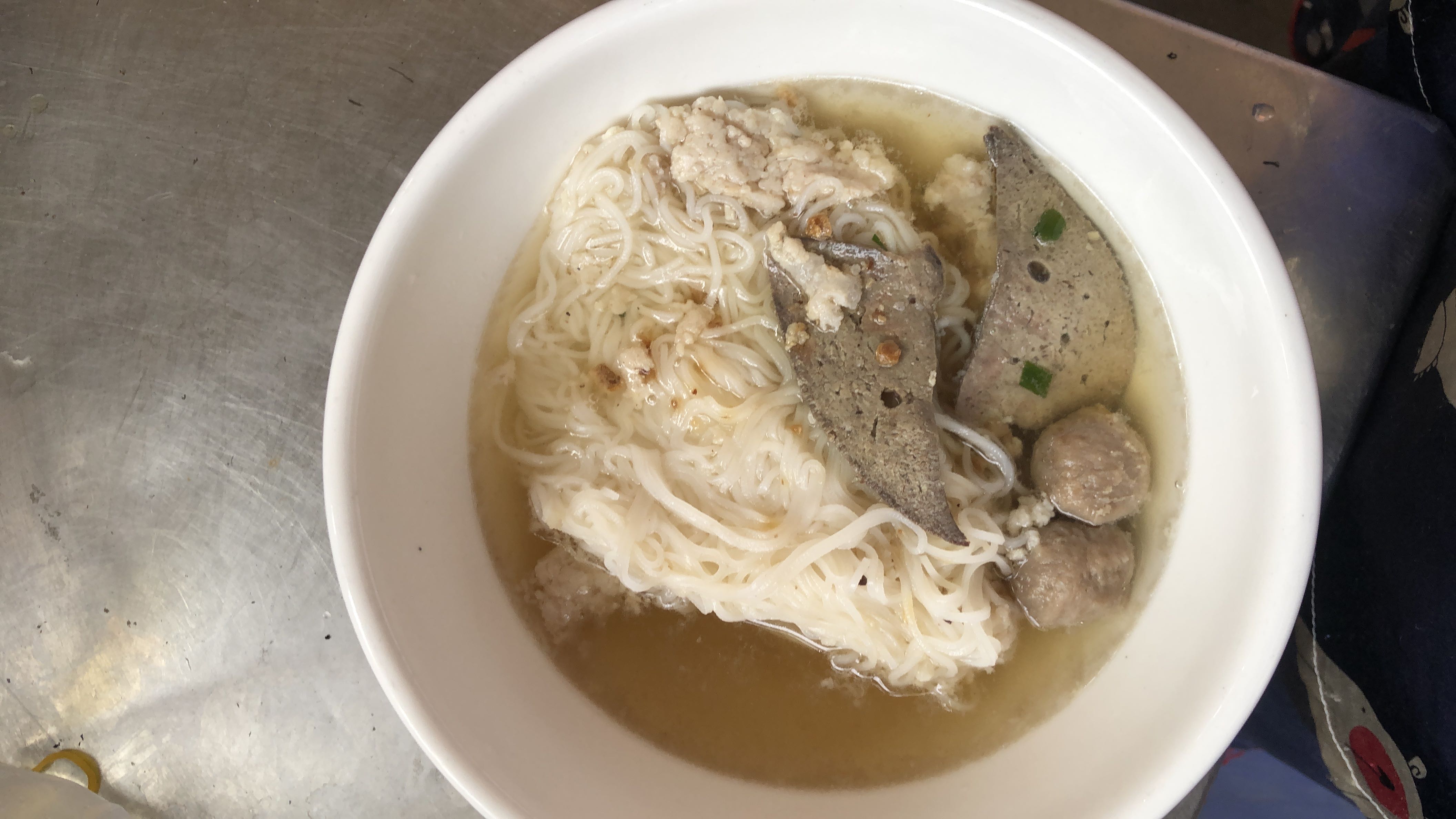 A bowl of rice noodles served in a clear broth with pork liver, meatballs, and minced pork.