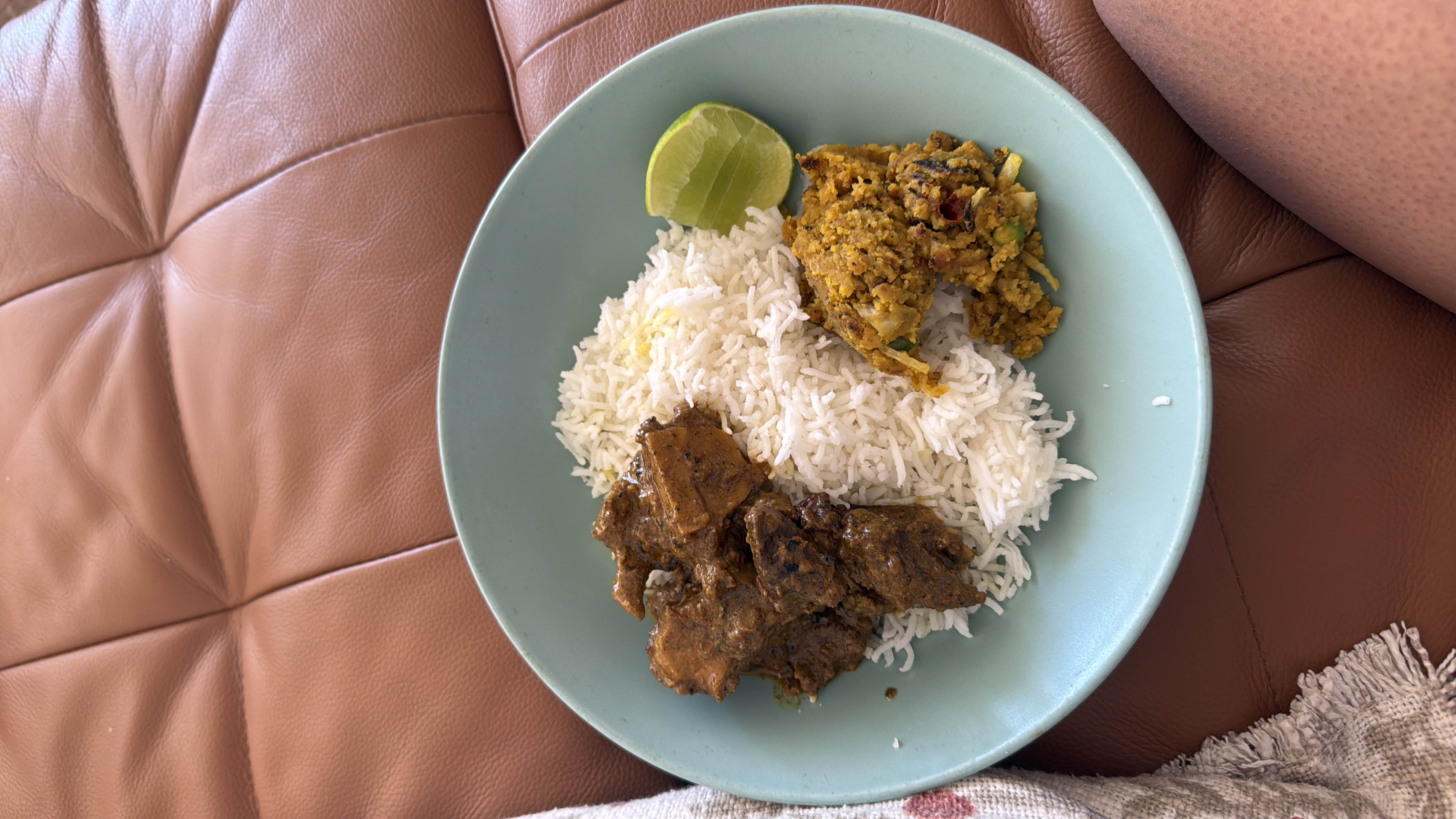 A balanced meal consisting of rice, meat curry, vegetable stir-fry, and a slice of lime.