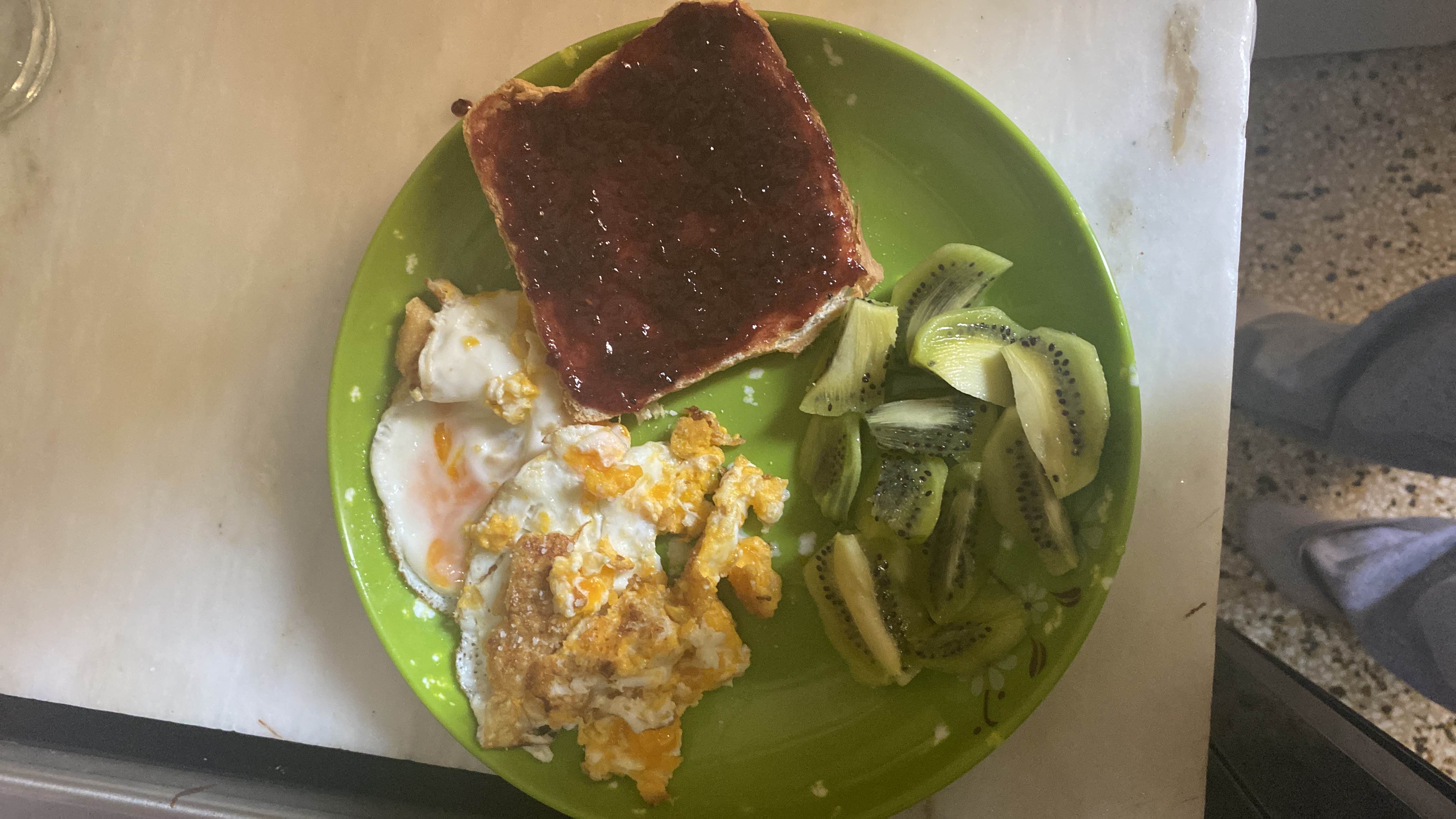 A balanced meal consisting of scrambled eggs, toast with jam, and sliced kiwi, providing a mix of protein, carbs, and vitamins.