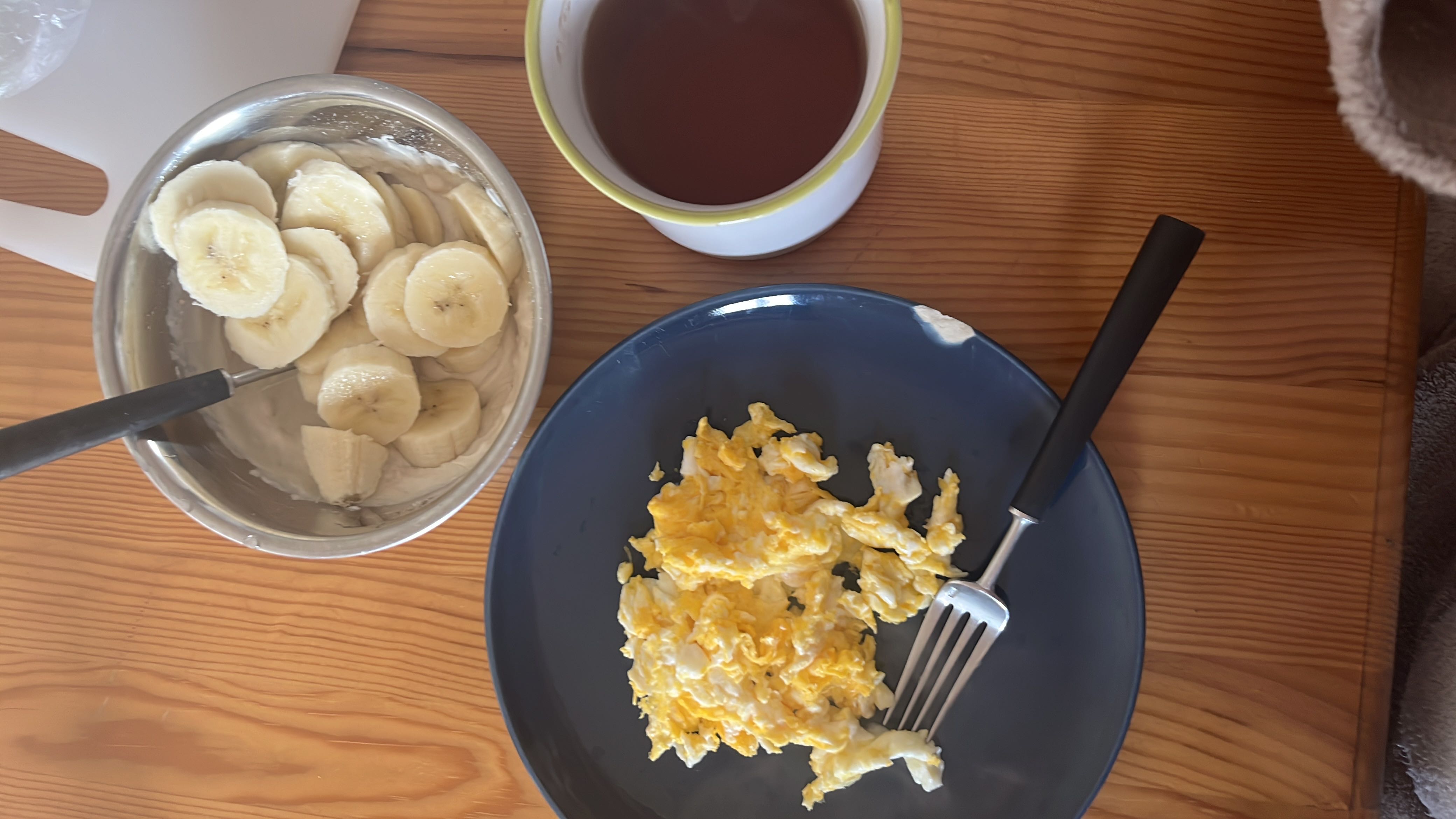 A balanced breakfast consisting of scrambled eggs, banana slices with yogurt, and a cup of tea.