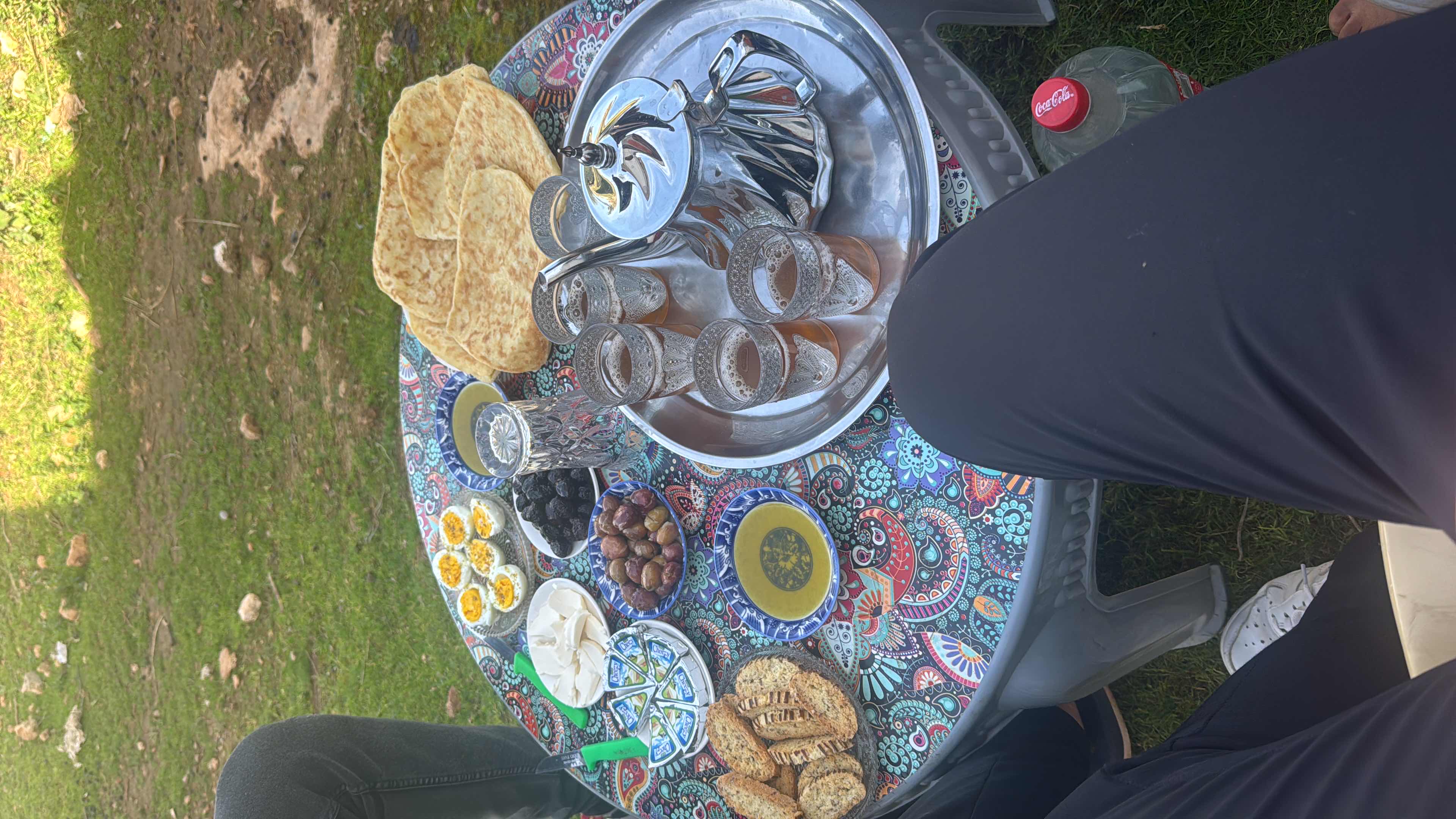 A traditional breakfast spread featuring bread, boiled eggs, olives, cheese, and tea, accompanied by olive oil and condiments.