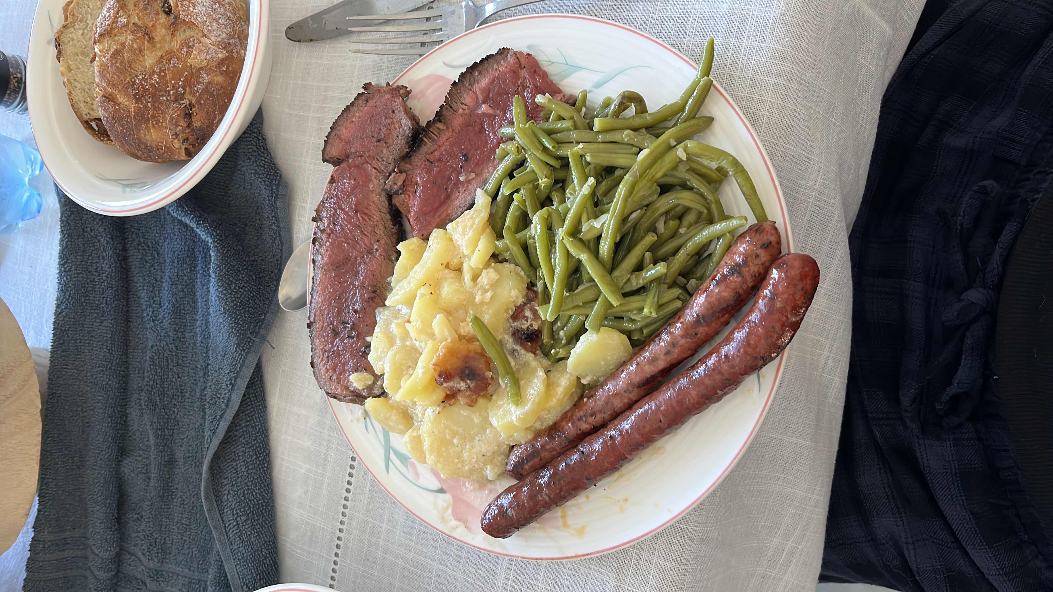 A balanced meal consisting of beef steak, sausages, green beans, potato gratin, and bread.